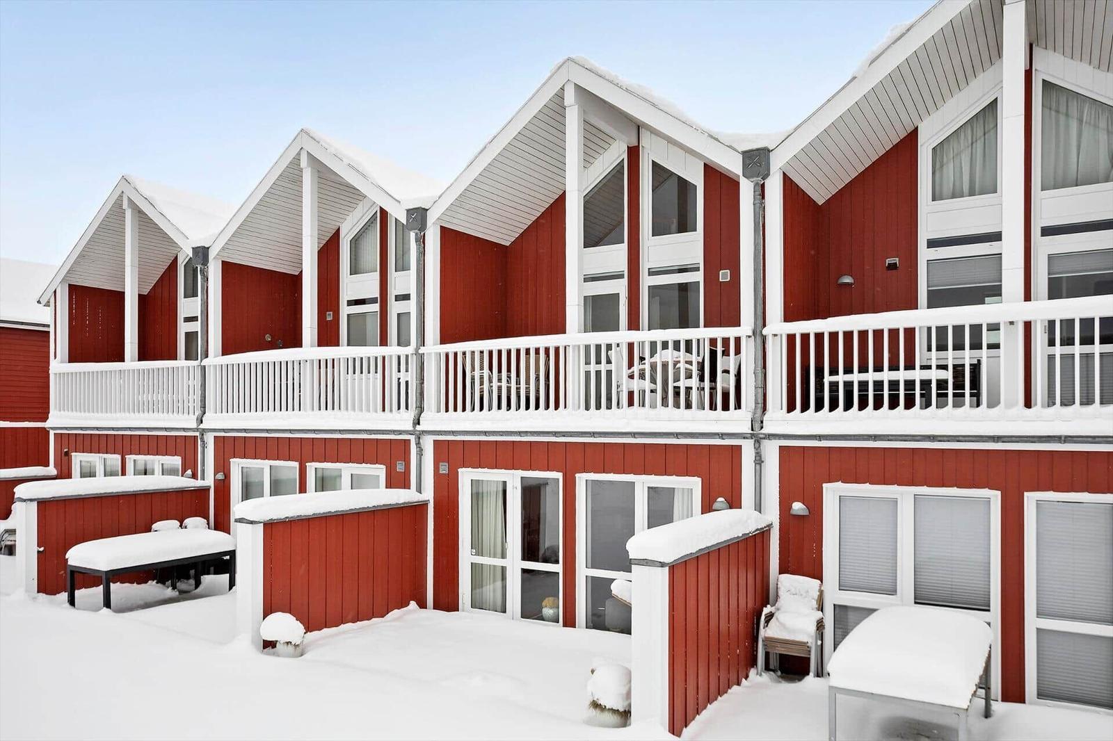 Red wooden houses with white balconies and snow on roofs and benches.