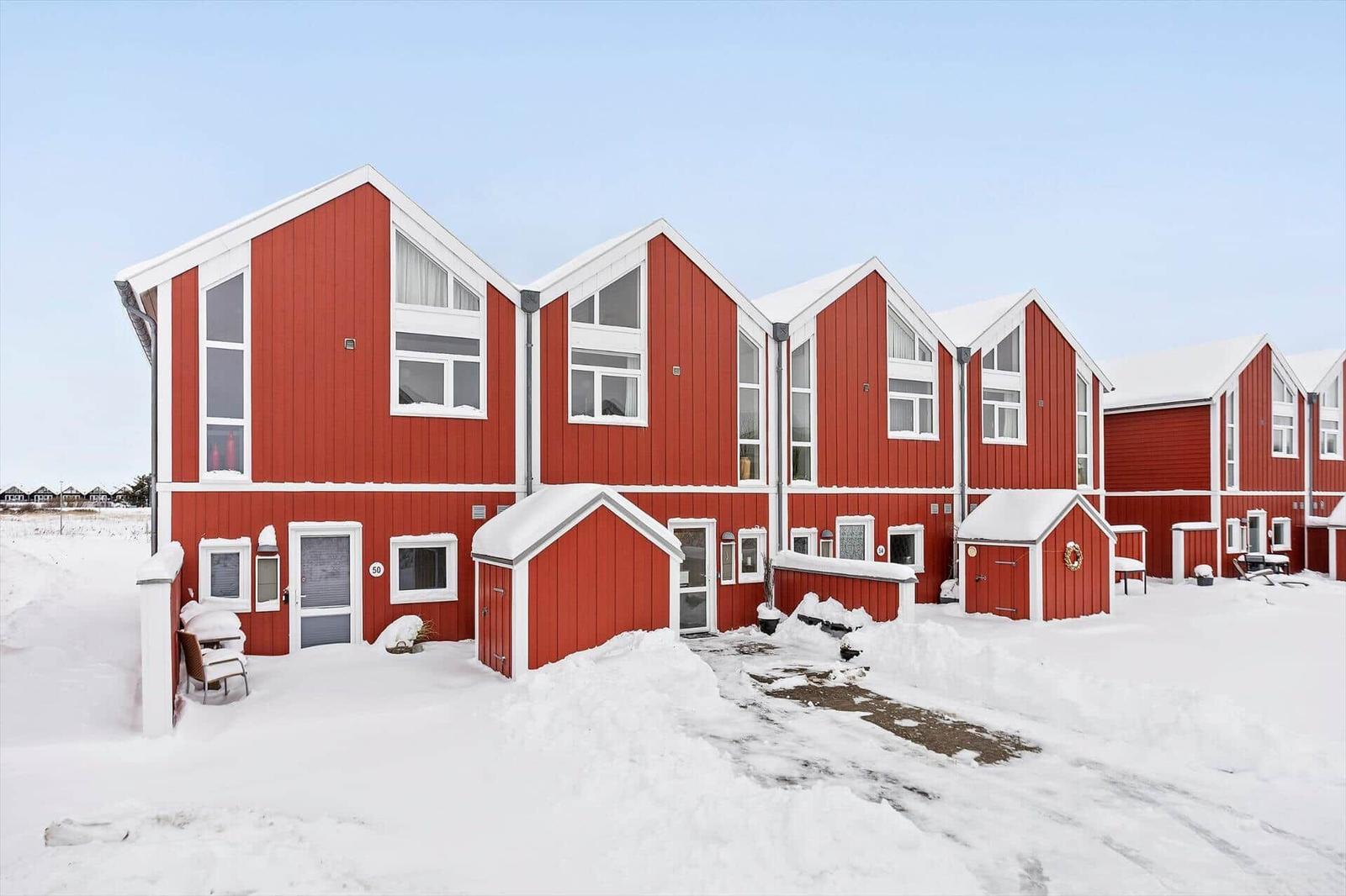 Red wooden houses with snow-covered roofs and small front yards in winter.