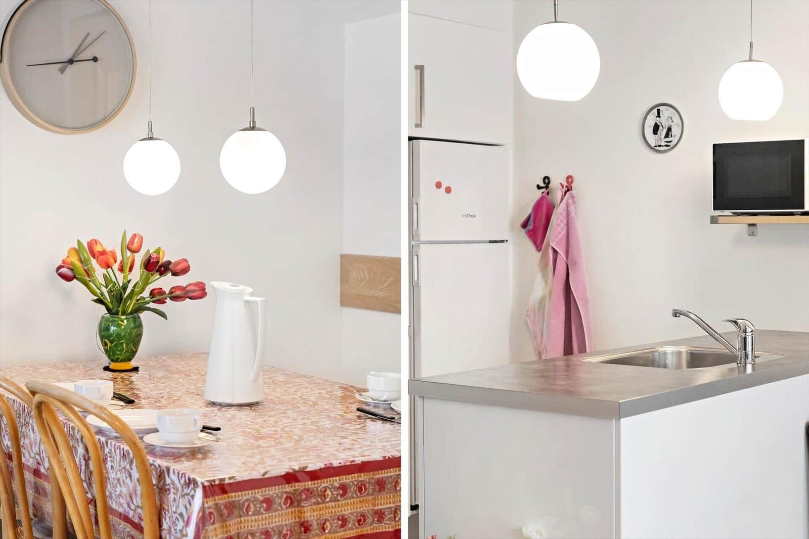 Dining table with flowers and kettle. Kitchen with sink, fridge, and microwave.