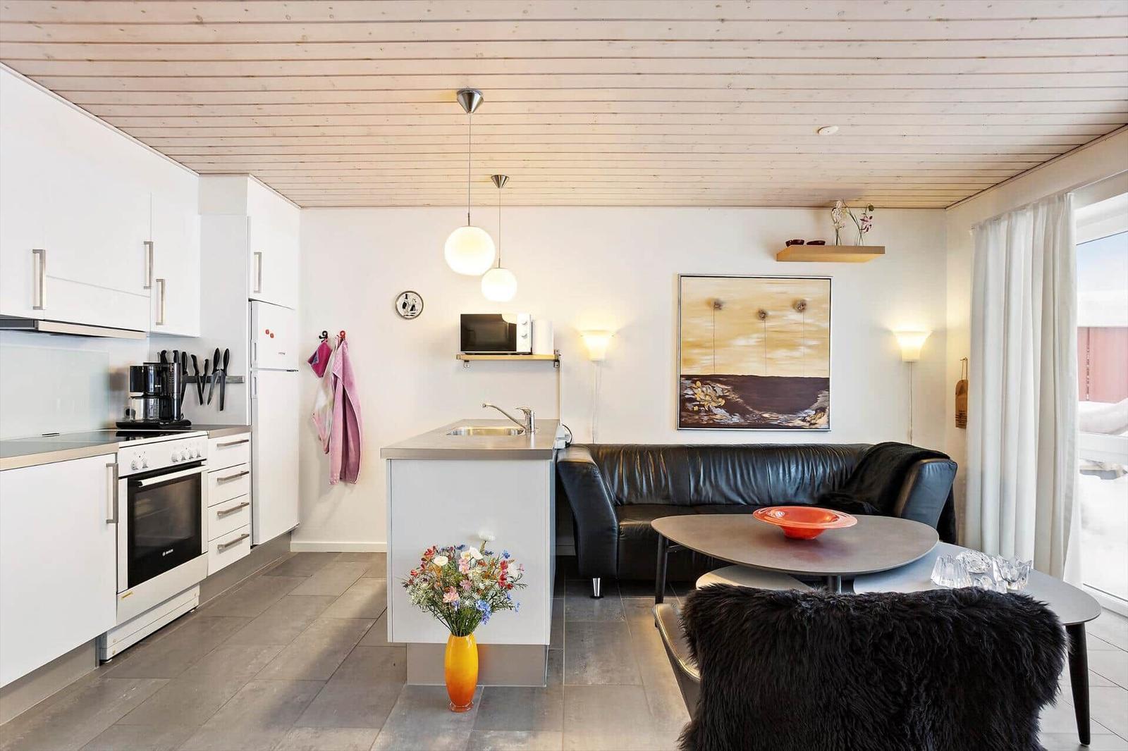 Kitchen and living area with black leather sofa, table, and wooden ceiling.
