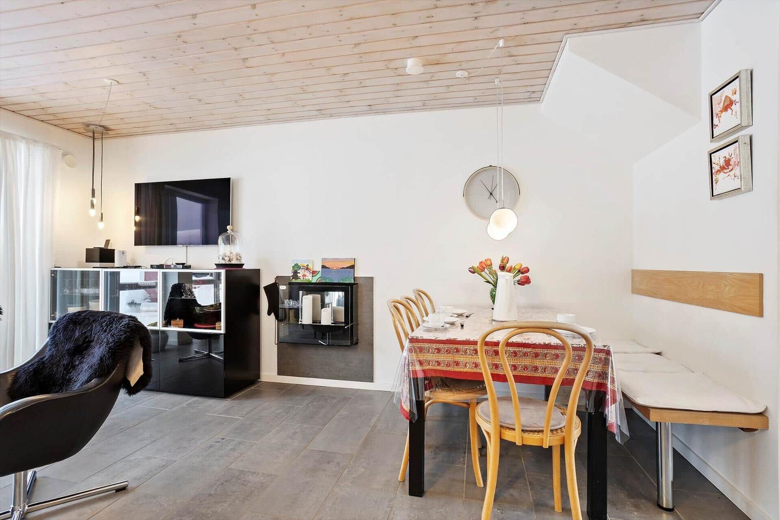 Dining area with table, chairs, and bench. TV and living area in background.