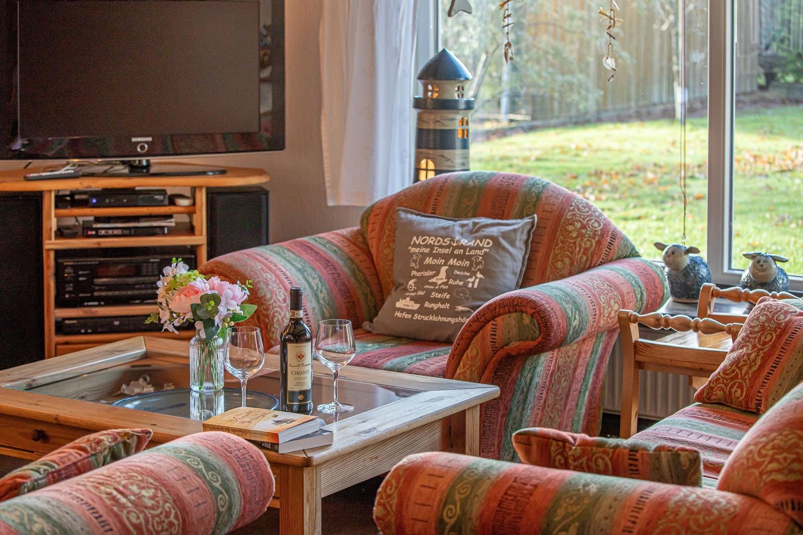 Wohnzimmer mit Sofa, Fernseher und Tisch mit Wein und Blumen.