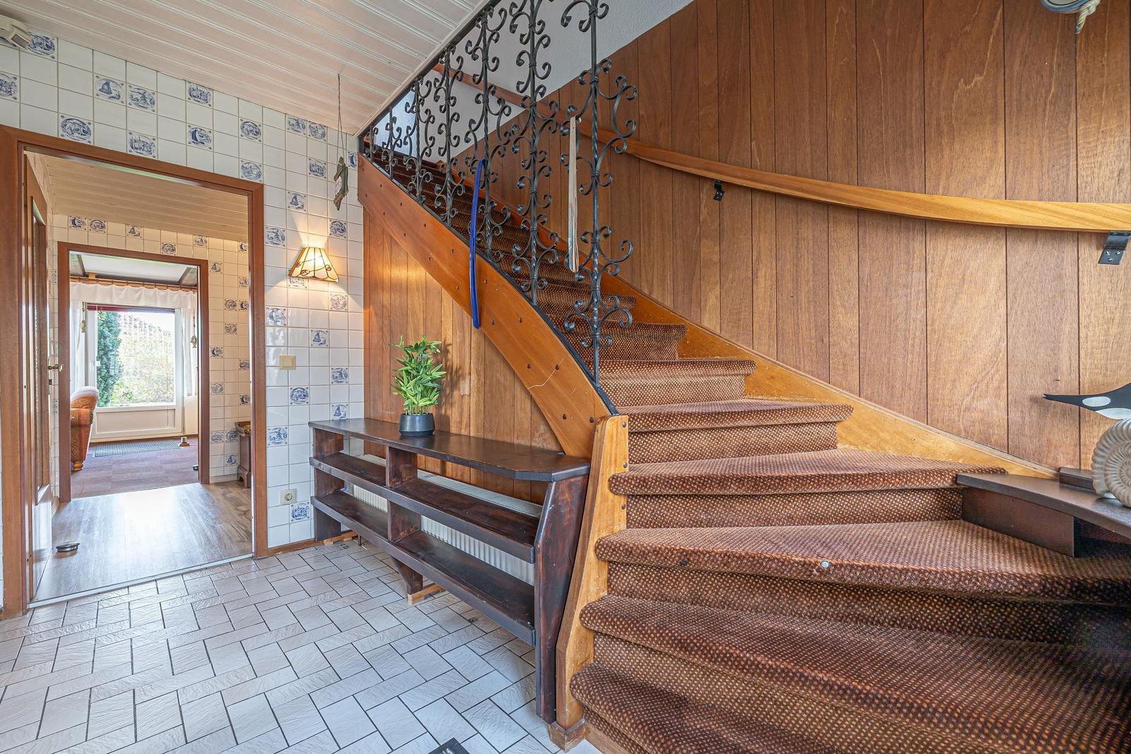 Haus mit Holztreppe, kunstvoller Metallgeländer und Fliesenwand im Eingangsbereich.