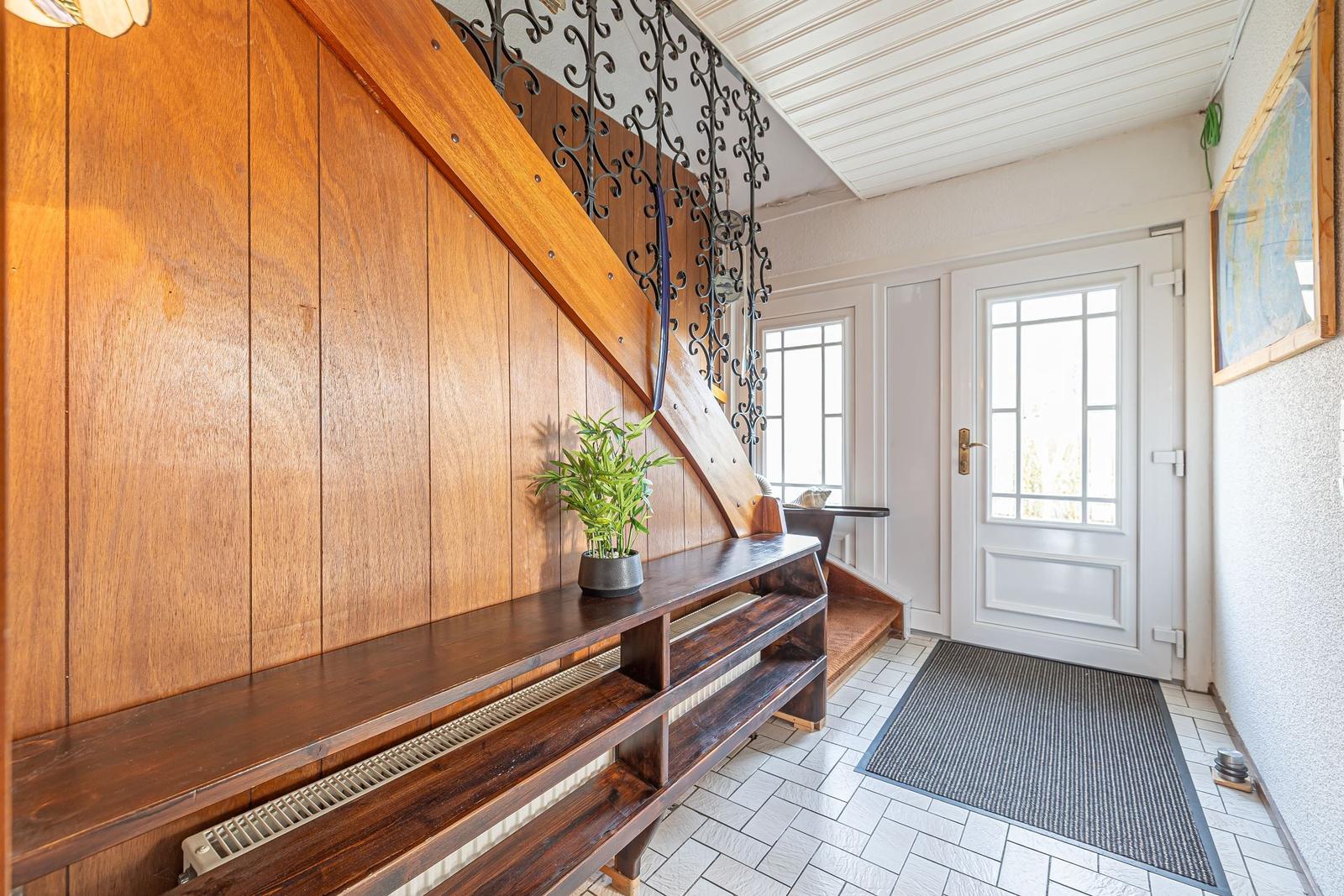 Eingangsbereich mit Holztreppe, Bänken und weißer Tür.