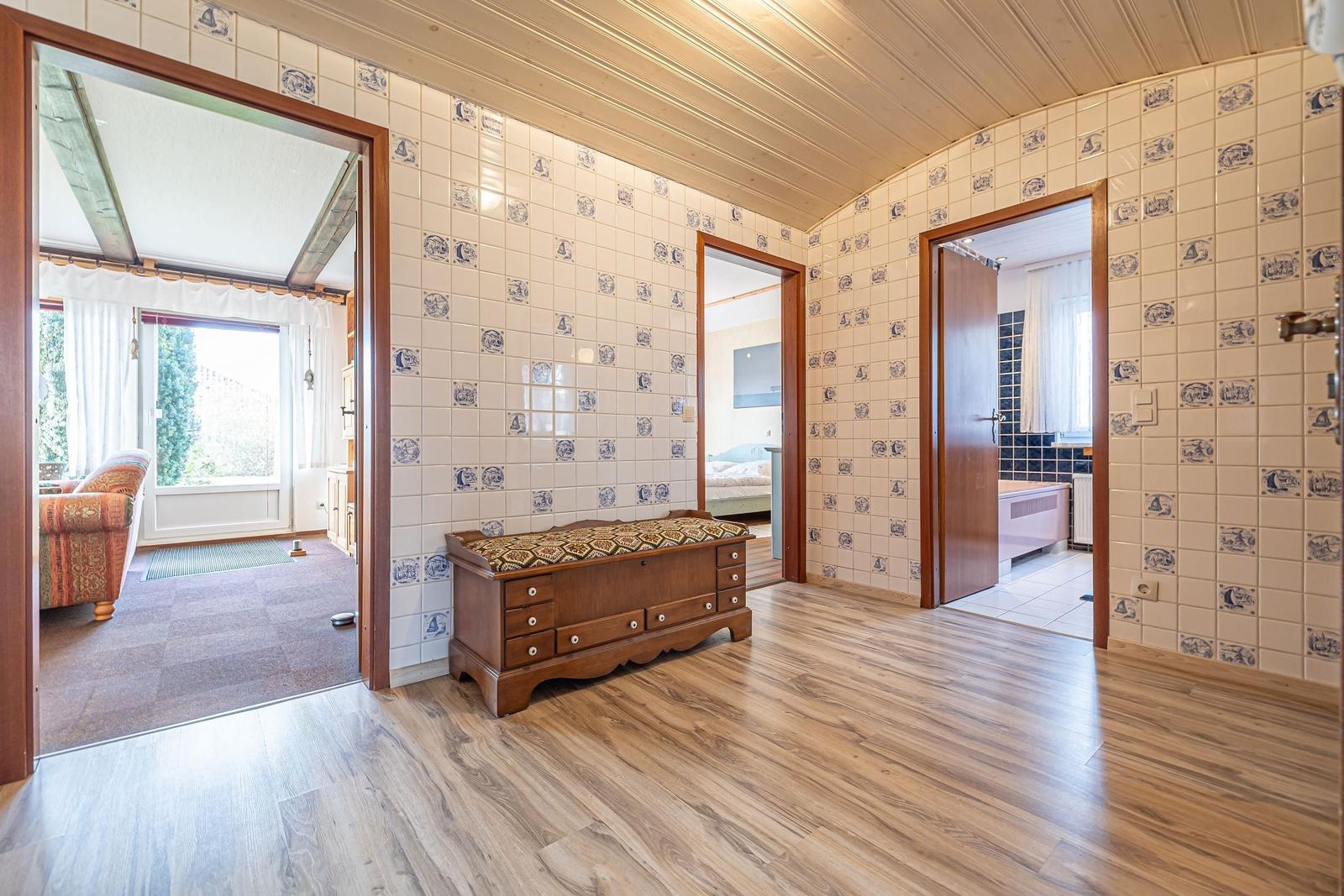 Raum mit Holzboden und Fliesenwand. Durchgänge zu Wohnzimmer, Schlafzimmer und Bad.