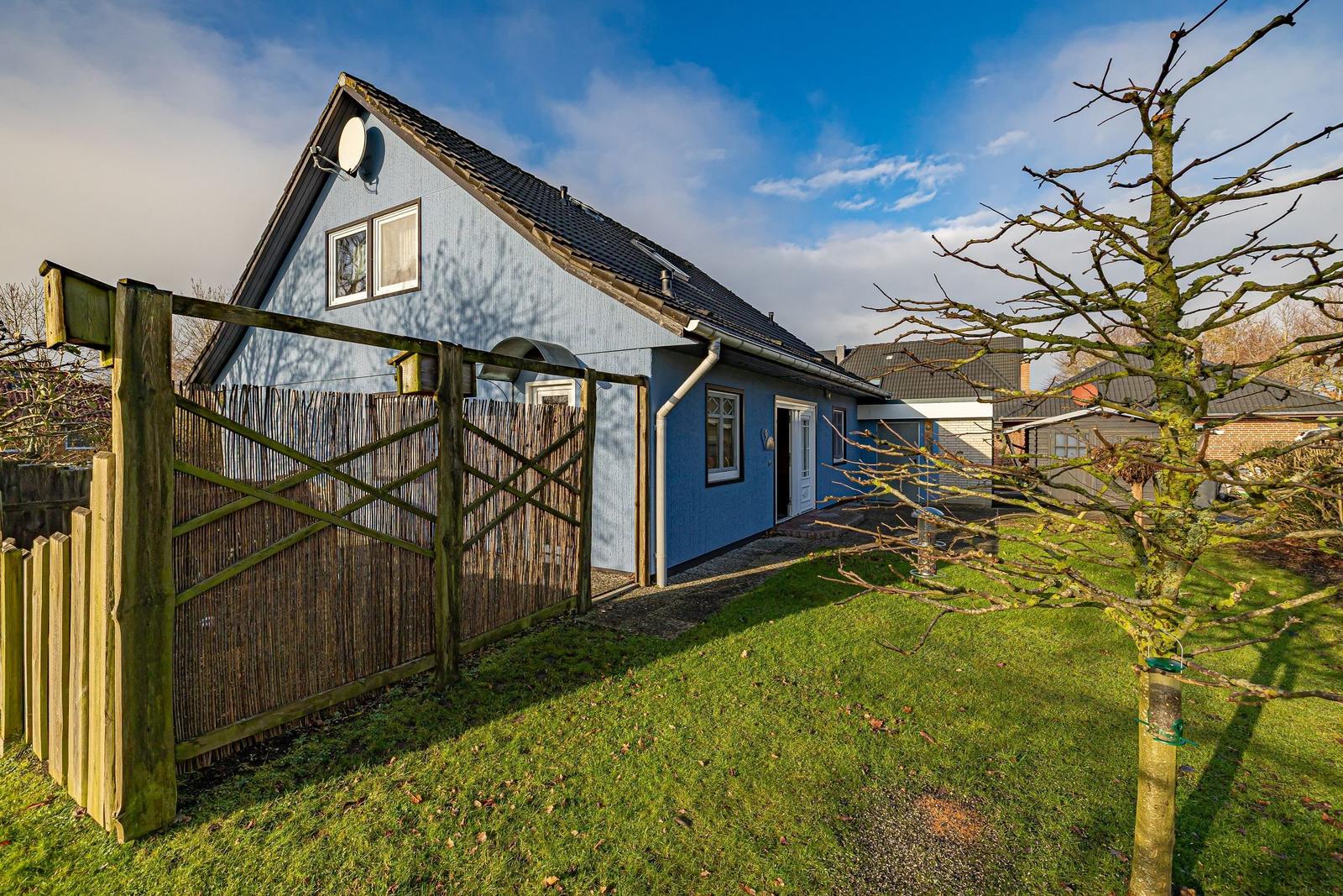Blauer Gartenhaus mit Holztor und Rasenfläche unter blauem Himmel.