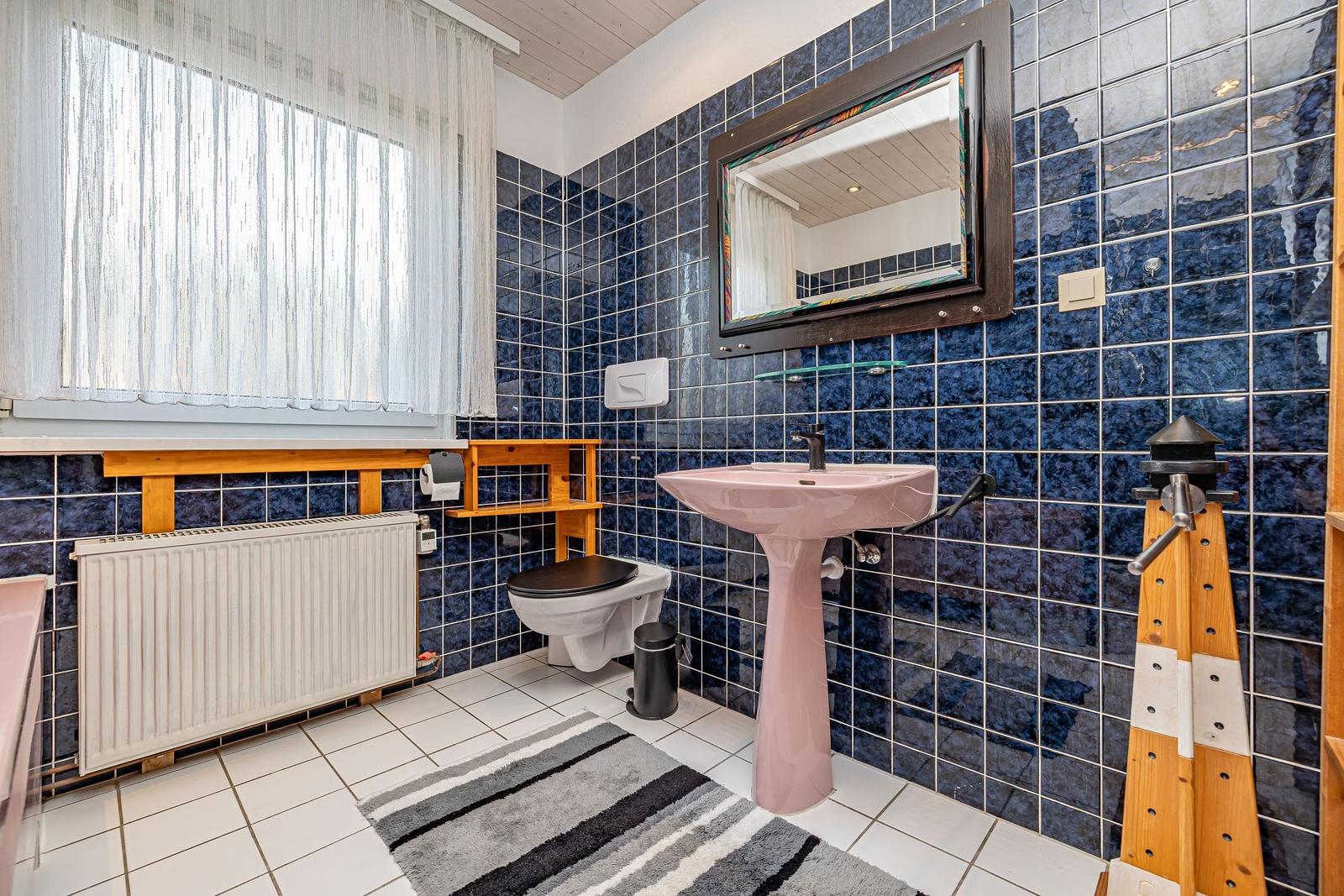 Badezimmer mit blauen Fliesen, rosa Waschbecken und Spiegel.
