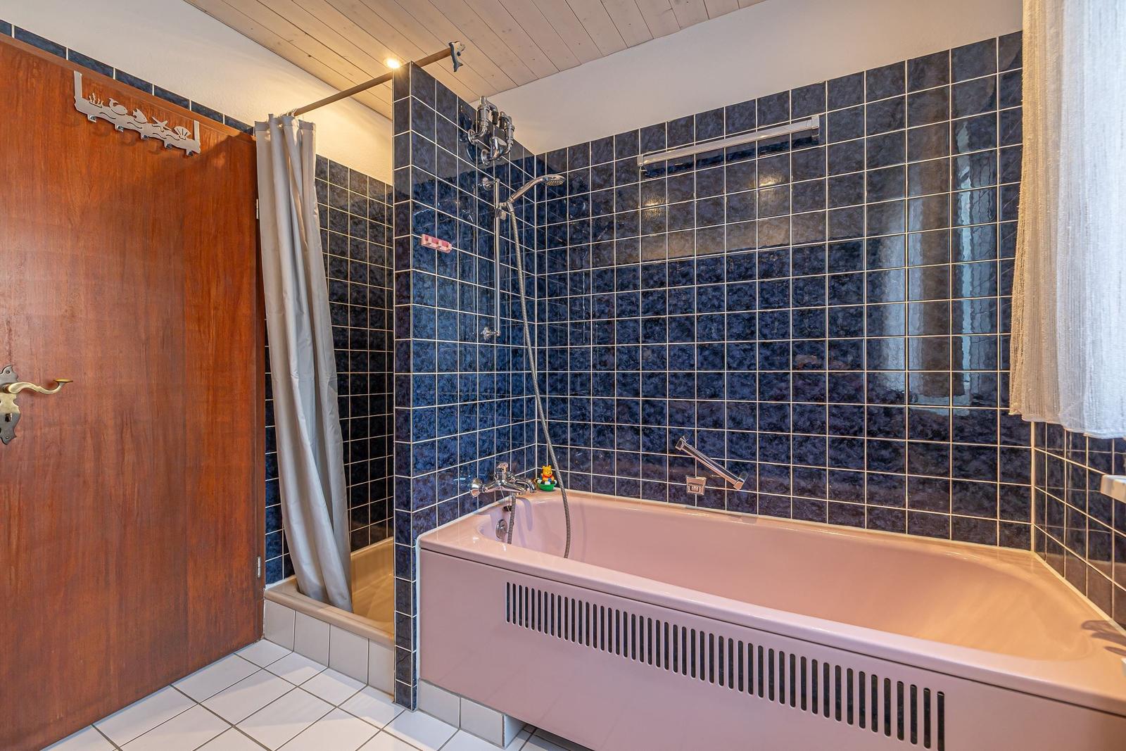 Bad mit Badewanne, Dusche und dunkelblauen Fliesen.