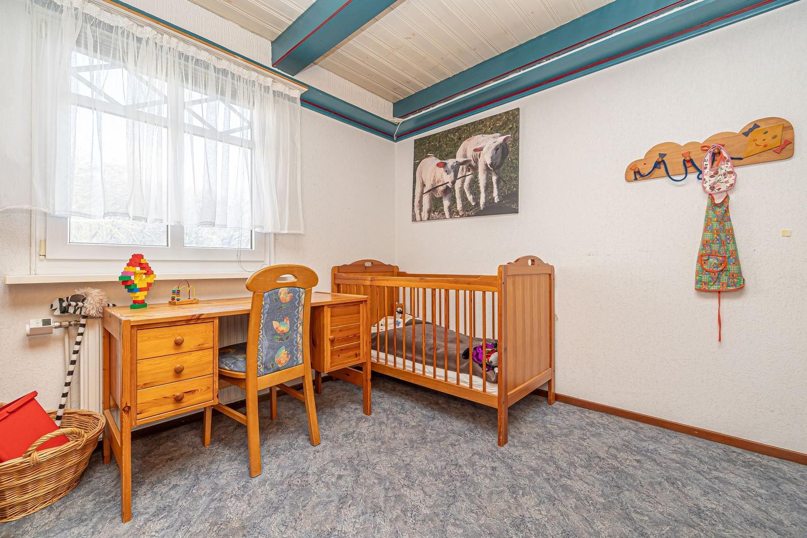 Ein Kinderzimmer mit Holz-Kinderbett, Schreibtisch und Wandbild von Schafen.