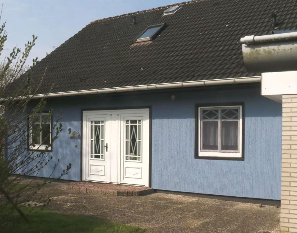 Blau gestrichenes Haus mit weißen Türen und Fenstern, Dach mit Dachfenstern.