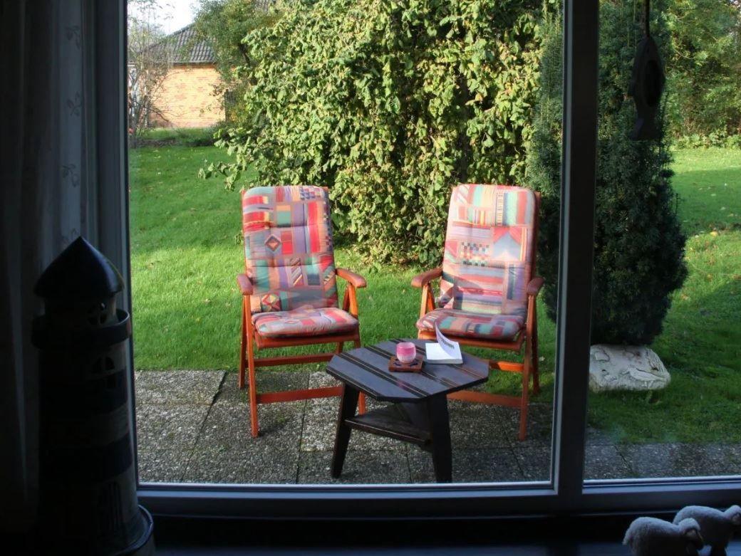 Zwei Stühle mit bunten Kissen und Tisch auf Terrasse mit Grünfläche und Hecke.