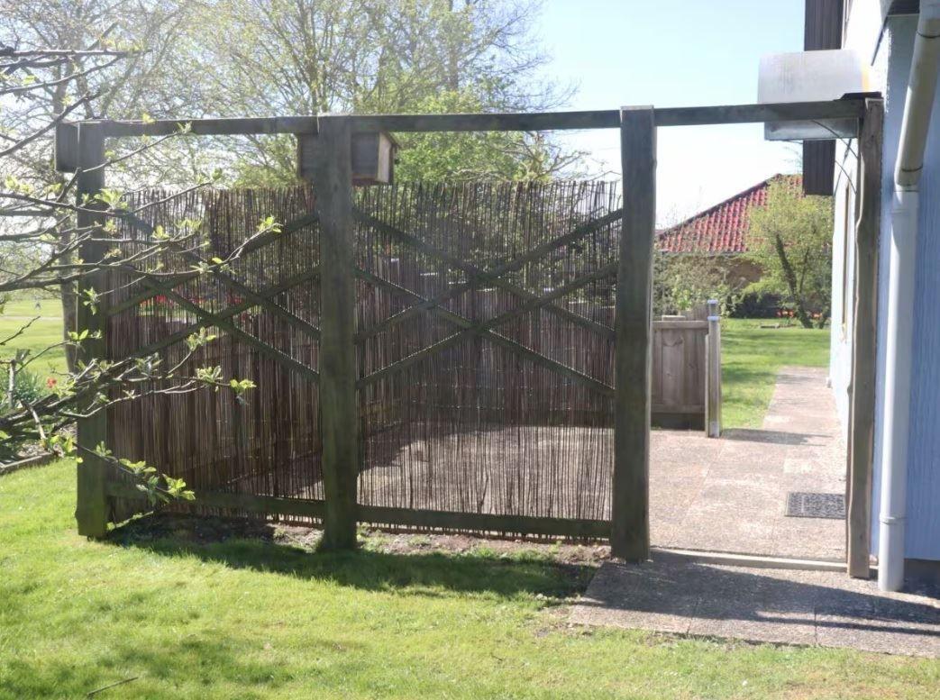 Holztor mit Bambuszaun führt zum Garten. Hinter dem Tor ist ein gepflasterter Weg.