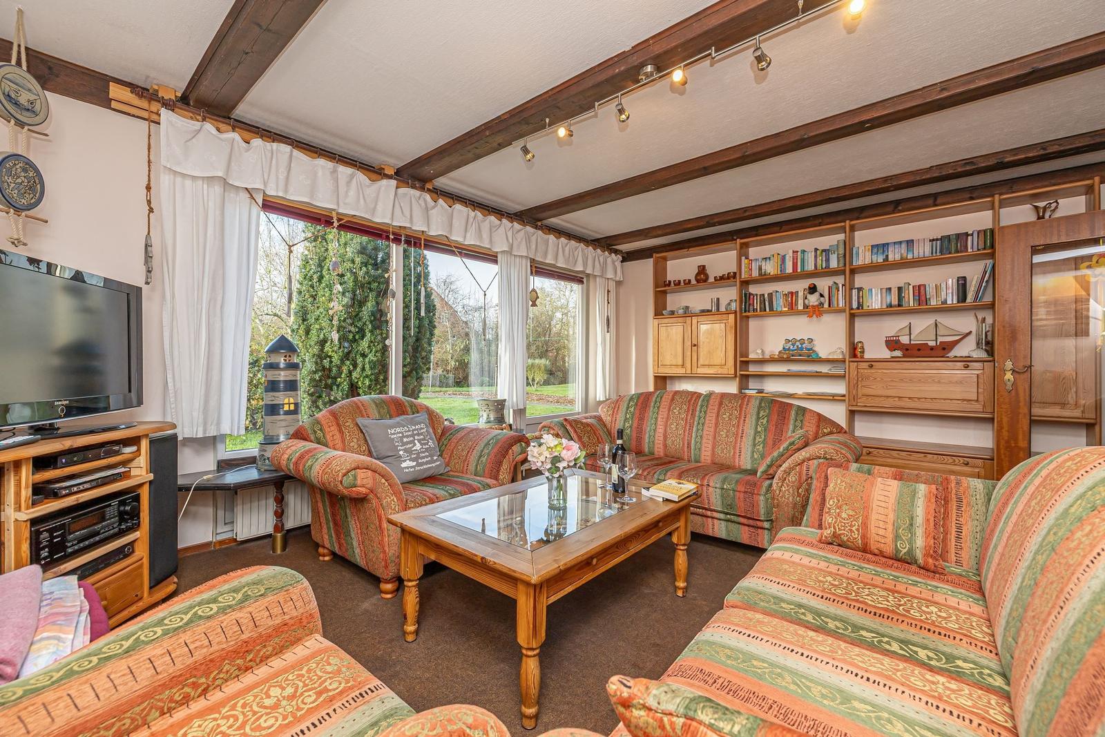 Wohnzimmer mit Sofa, Fernseher und Bücherregal. Blick auf Garten durch Fenster.