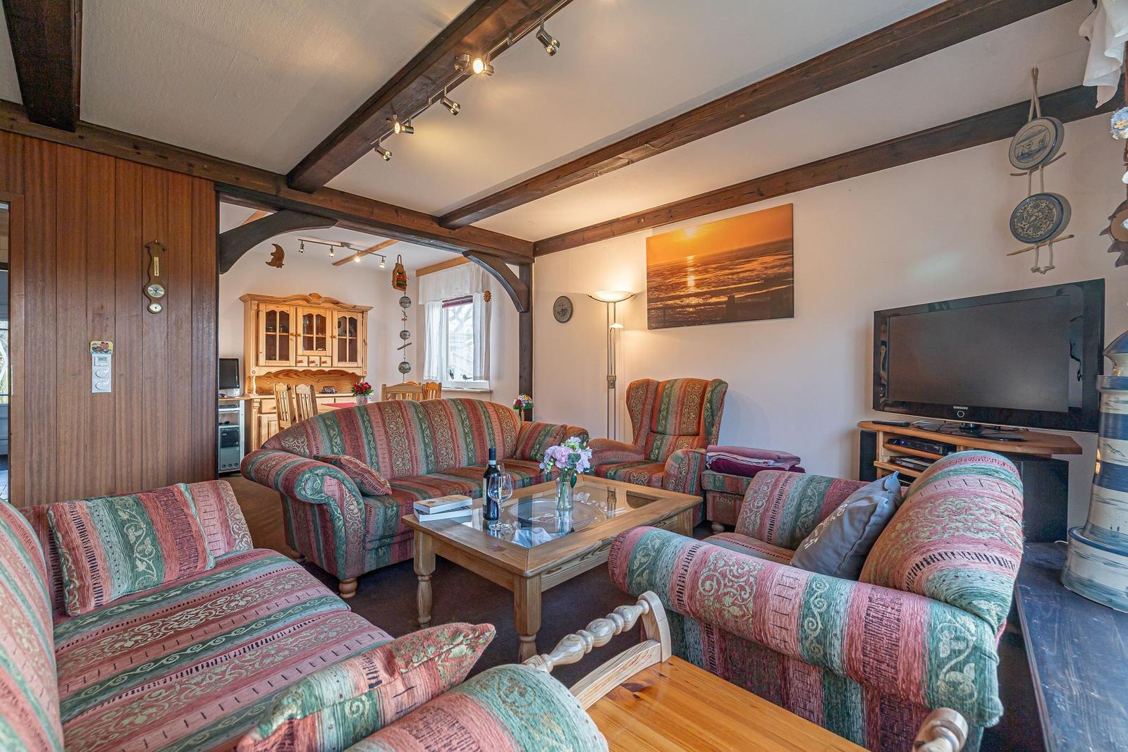 Wohnzimmer mit Sofa, Sessel und Fernseher. Holzrahmen und Glasplatte.