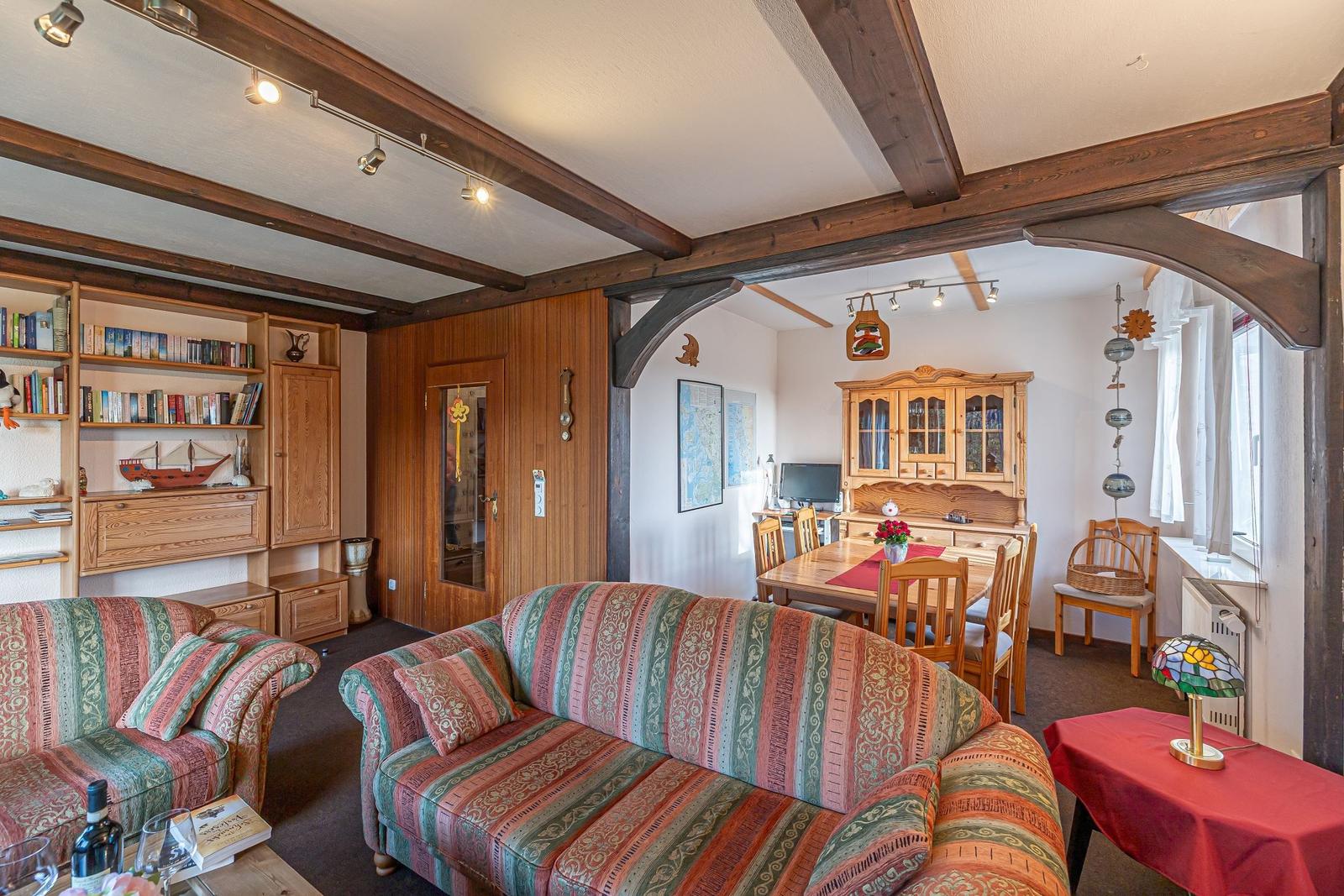 Wohn- und Essbereich mit Holzbalken, Sofa, Esstisch und Bücherregal.