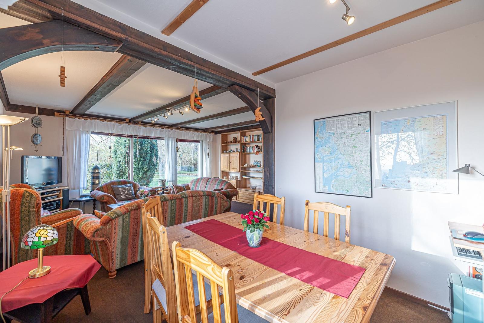 Essbereich mit Holztisch, Stühlen und Karte an der Wand. Wohnbereich mit Sofa und Fernseher.