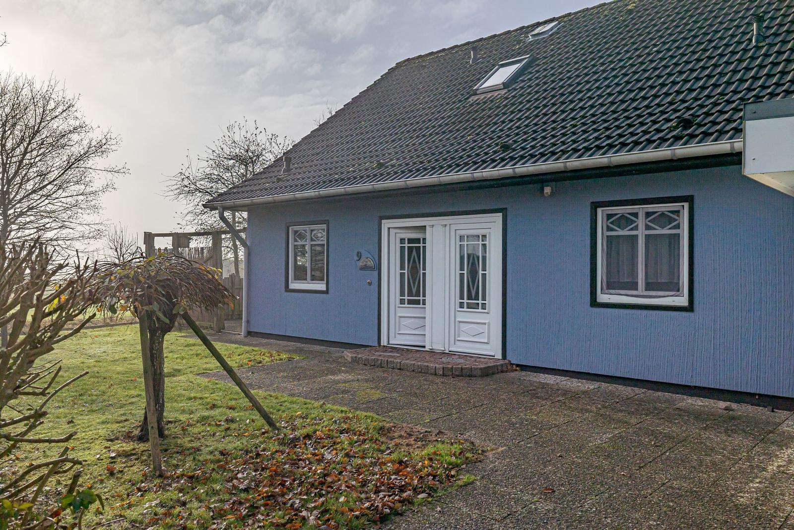 Blauer Einfamilienhaus mit weißen Fenstern und Tür. Vorgarten mit Rasen und Bäumen.