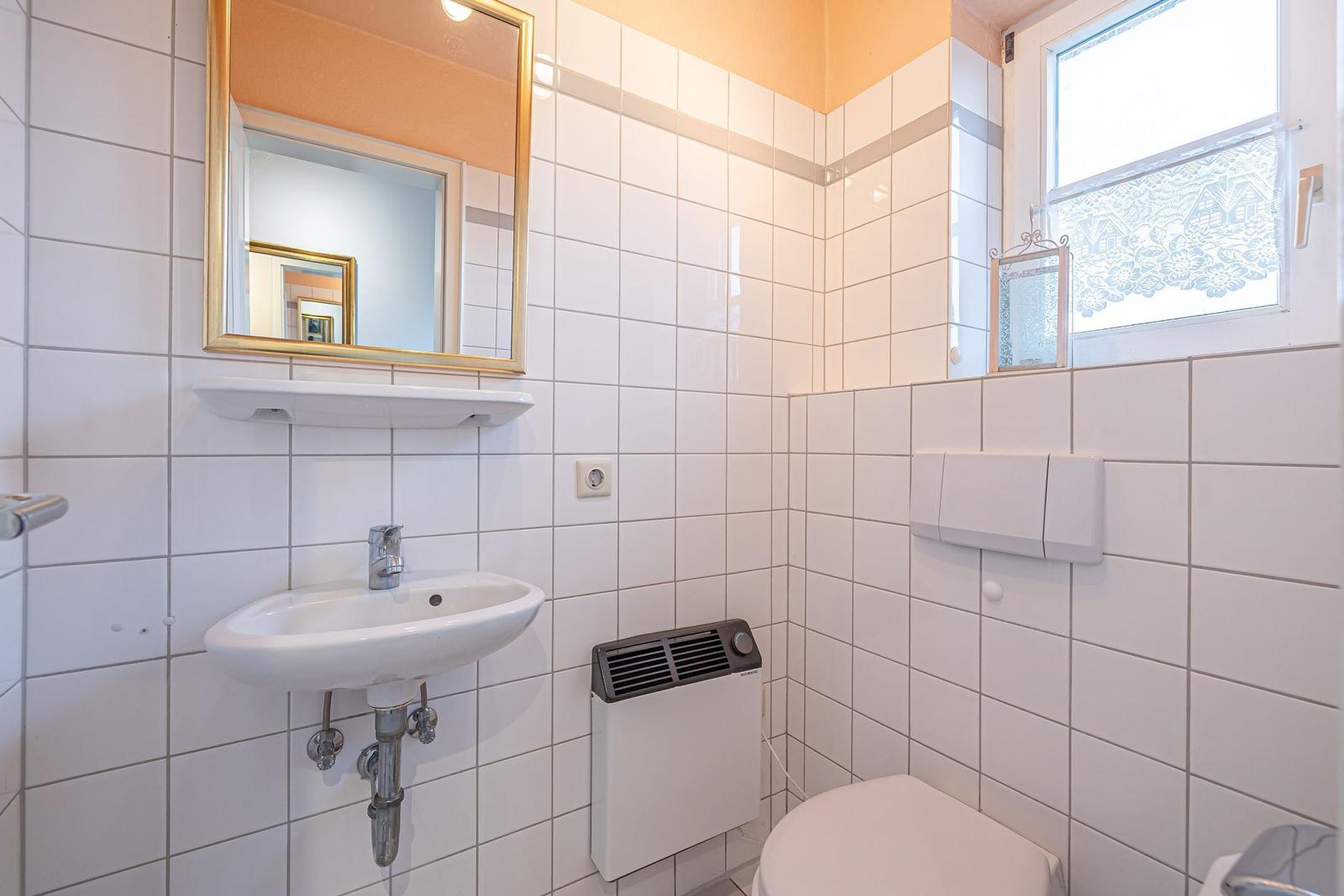 Badezimmer mit Waschbecken, Spiegel, Toilette und Fenster mit Vorhang.