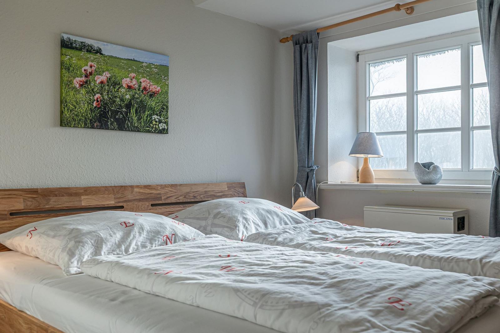 Schlafzimmer mit Bett, Fenster und Wandbild.