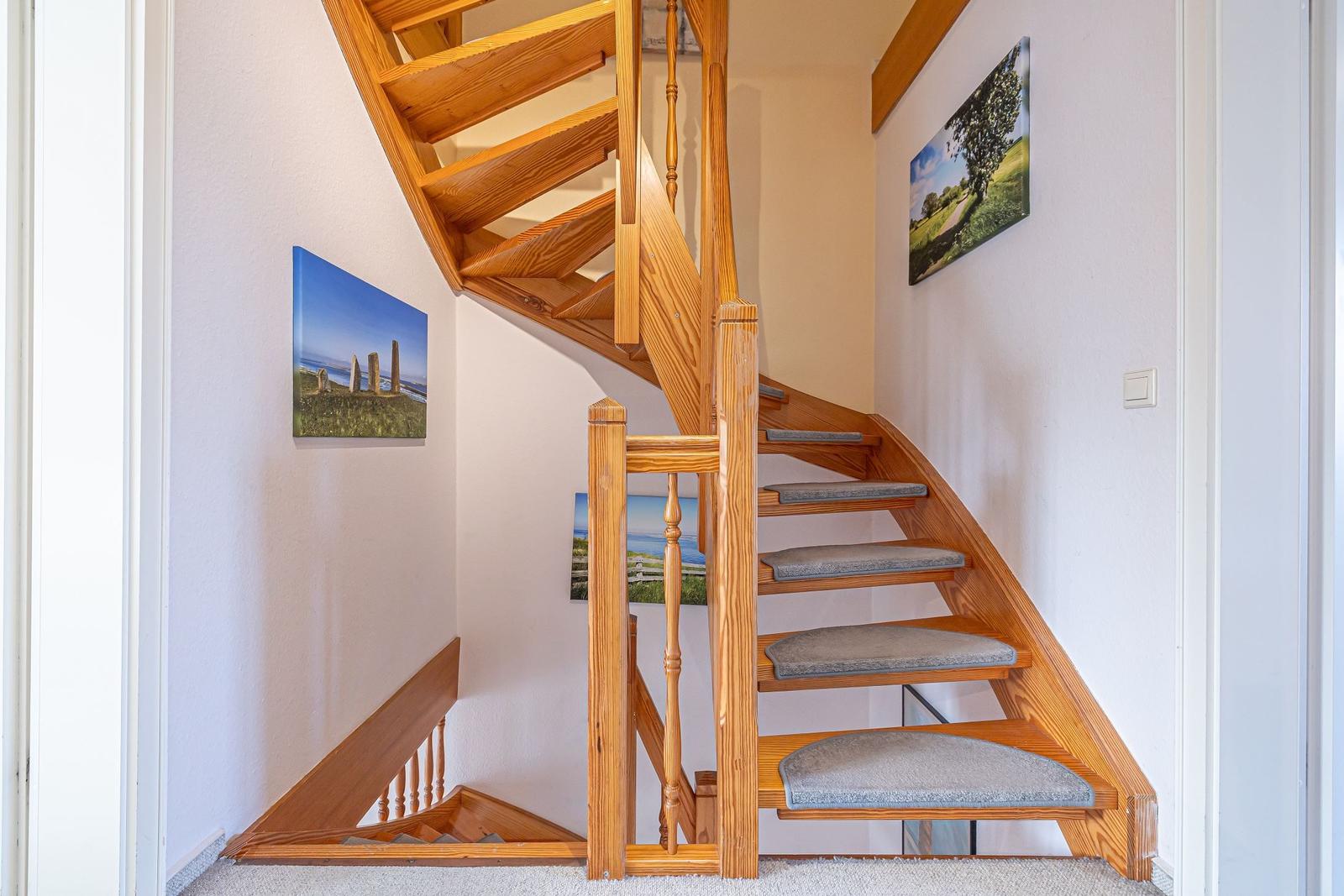 Holz-Treppe mit grauen Stufenbezug, Wandbilder und weißer Wand.