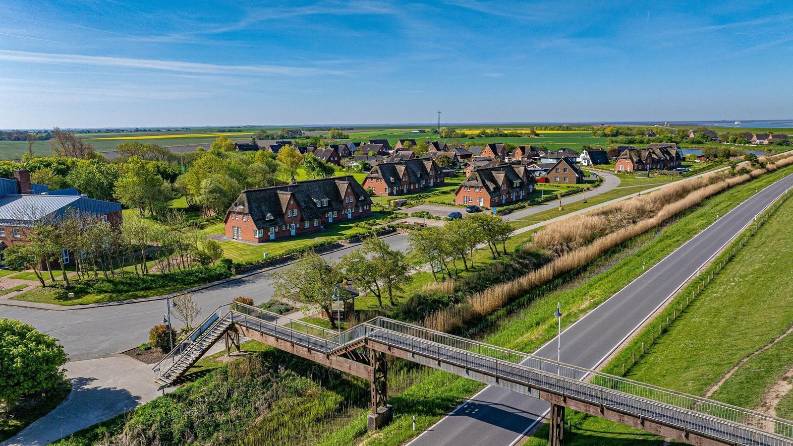 Dorf mit roten Häusern und grünen Wiesen unter blauem Himmel.
