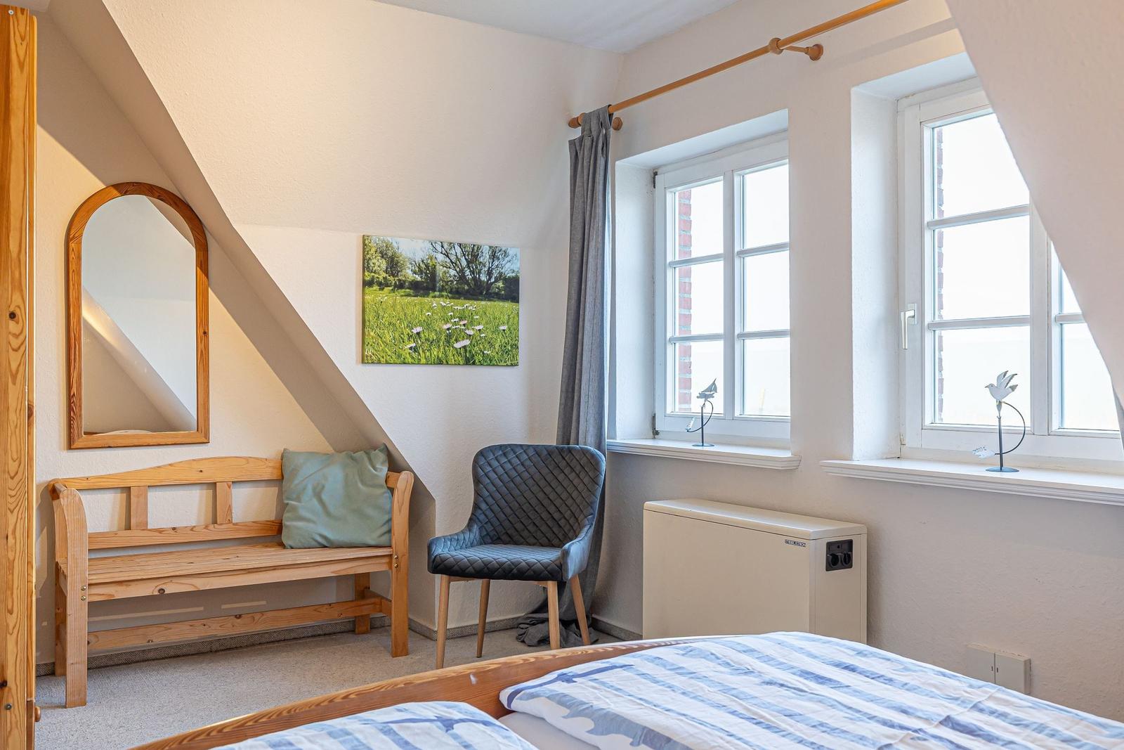 Schlafzimmer mit Dachschrägen, Bett, Bank, Stuhl und Fenster.