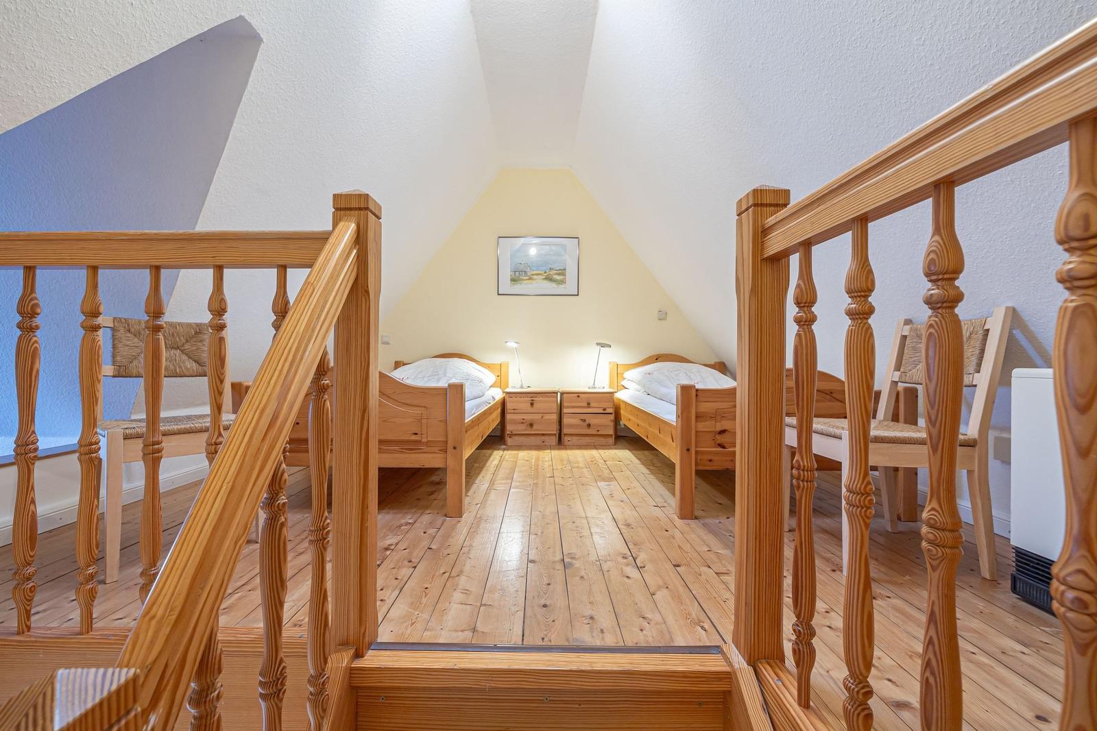 Zwei Einzelbetten mit Nachttischen unter einem Dachfenster. Holzboden und Holzgeländer.