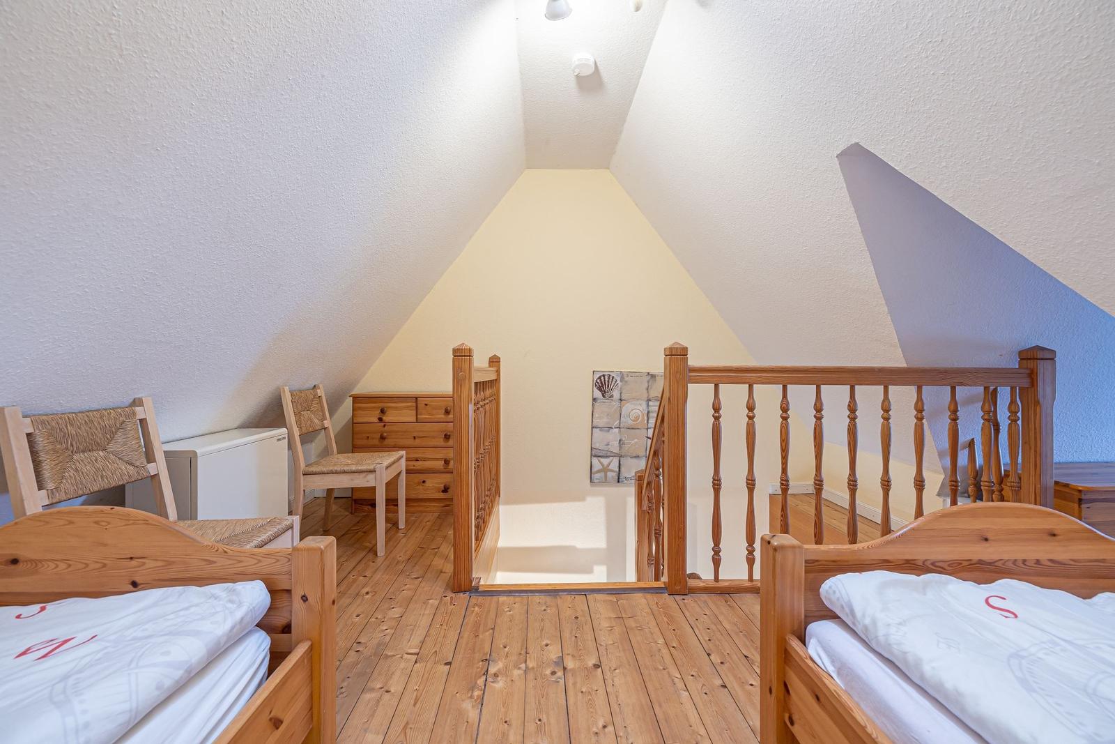 Zimmer mit zwei Betten, Holzboden und Dachschrägen. Holzgeländer und Kleiderschrank sichtbar.
