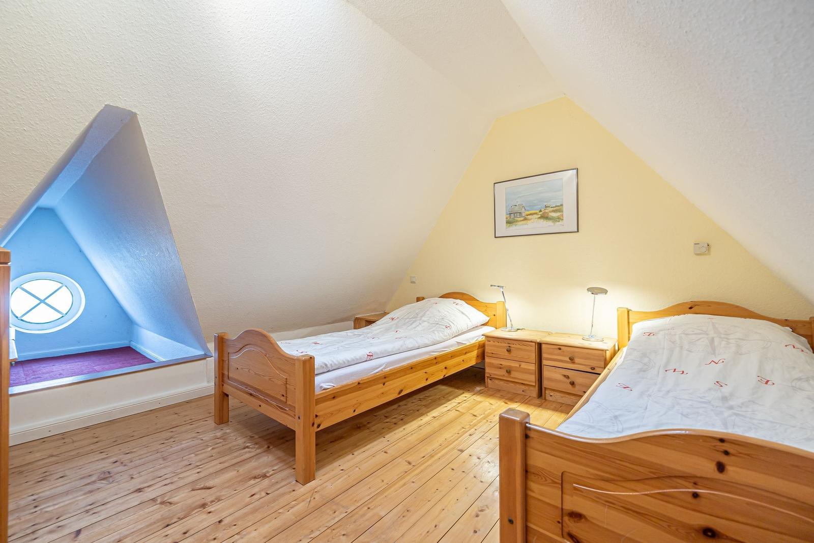 Zwei Einzelbetten, Holzboden und ein Fenster im Dachgeschosszimmer.