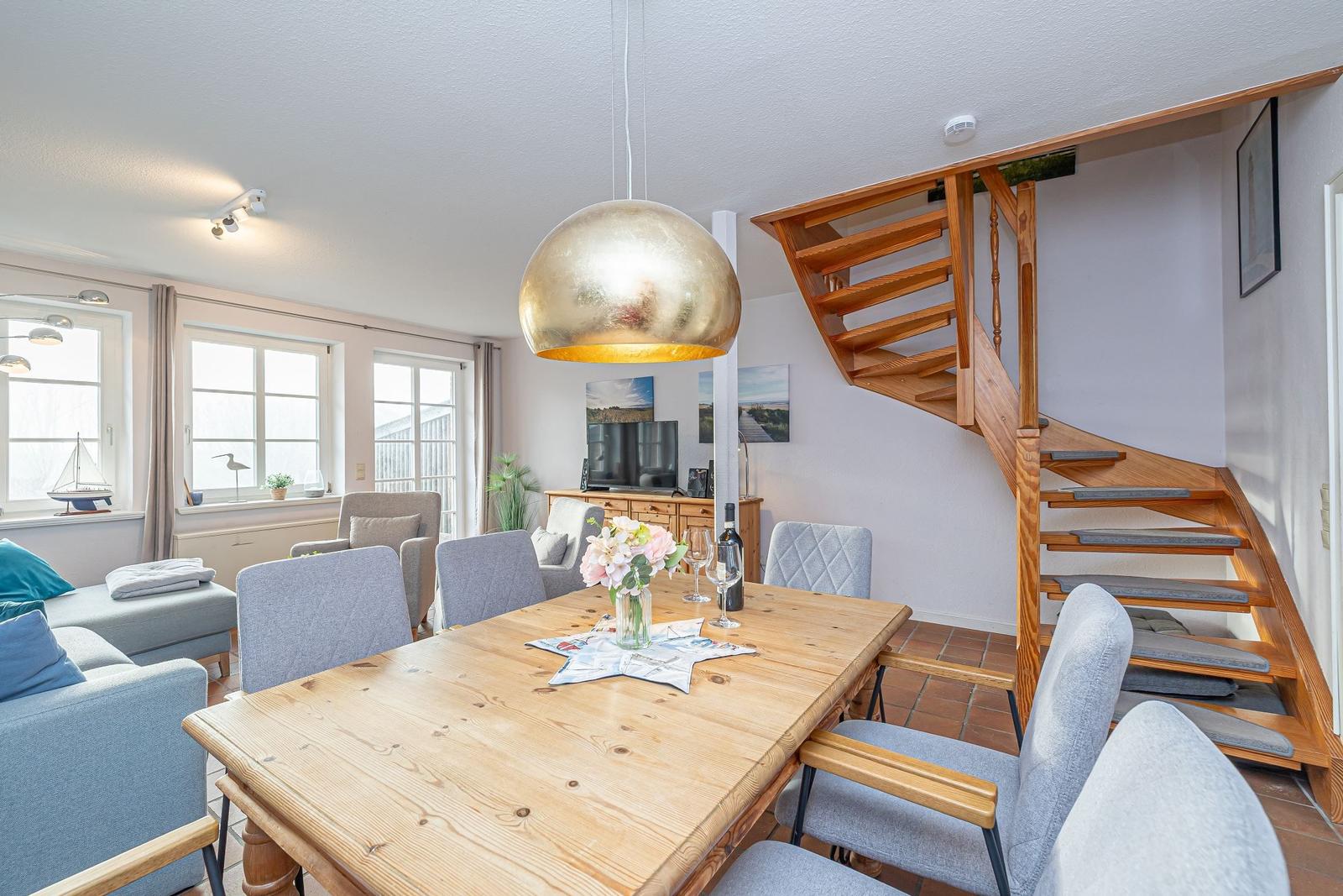 Essbereich mit Holztisch, grauen Stühlen und goldenem Hängelampen. Holz-Treppe führt nach oben.