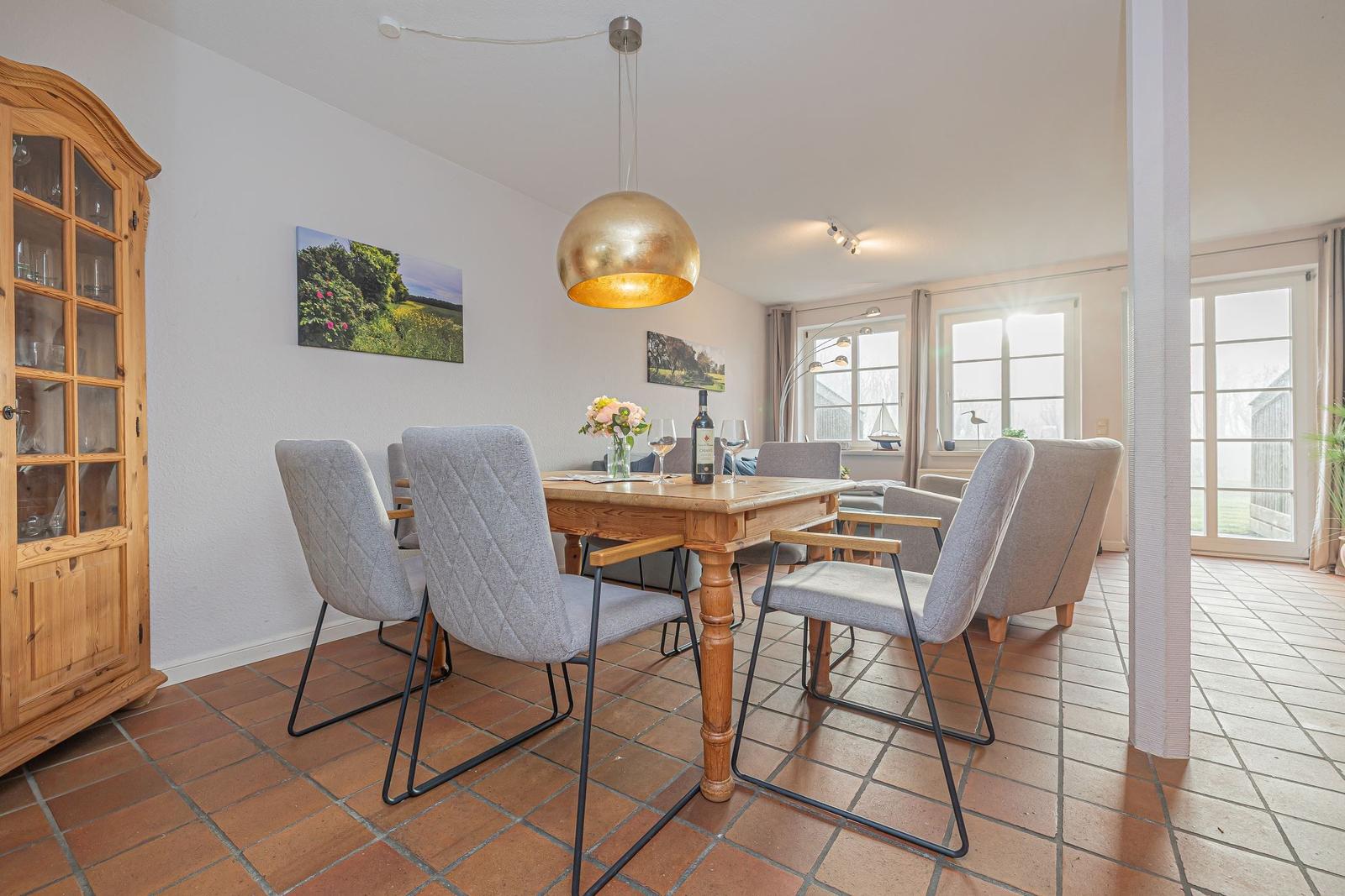 Esszimmer mit Holztisch, grauen Stühlen und goldener Pendelleuchte. Terrakottafußboden und Fenster zur Terrasse.