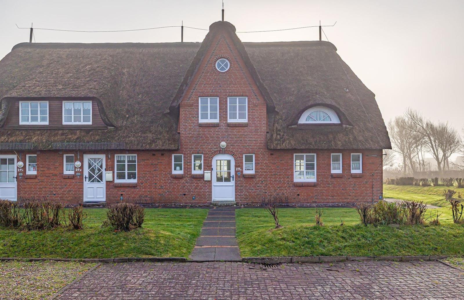 Rotes Backsteingebäude mit Strohdach und weißen Fenstern. Vorgarten mit Weg und Gras.