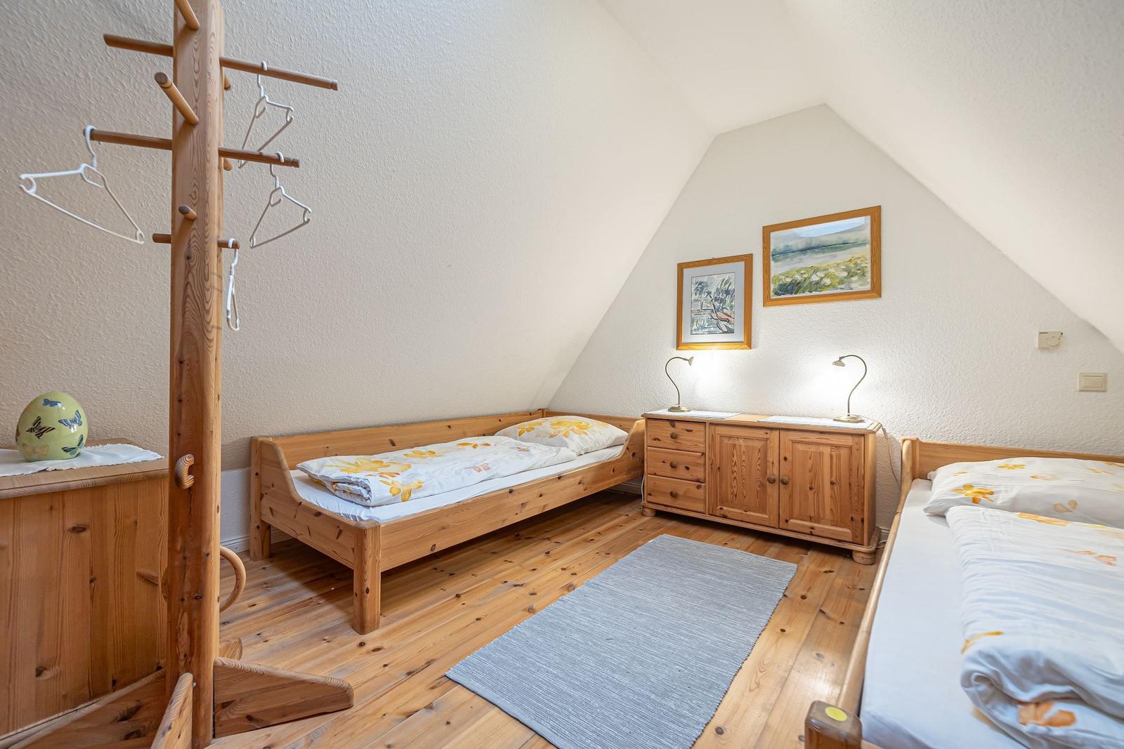 Zimmer mit zwei Betten, Holzmöbel und Schrägdach. Holzfußboden und Teppich.