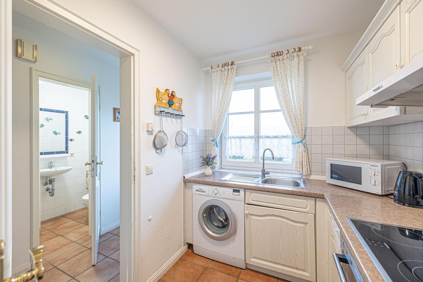 Küche mit Waschmaschine, Spüle und Fenster. Badezimmer ist angrenzend.