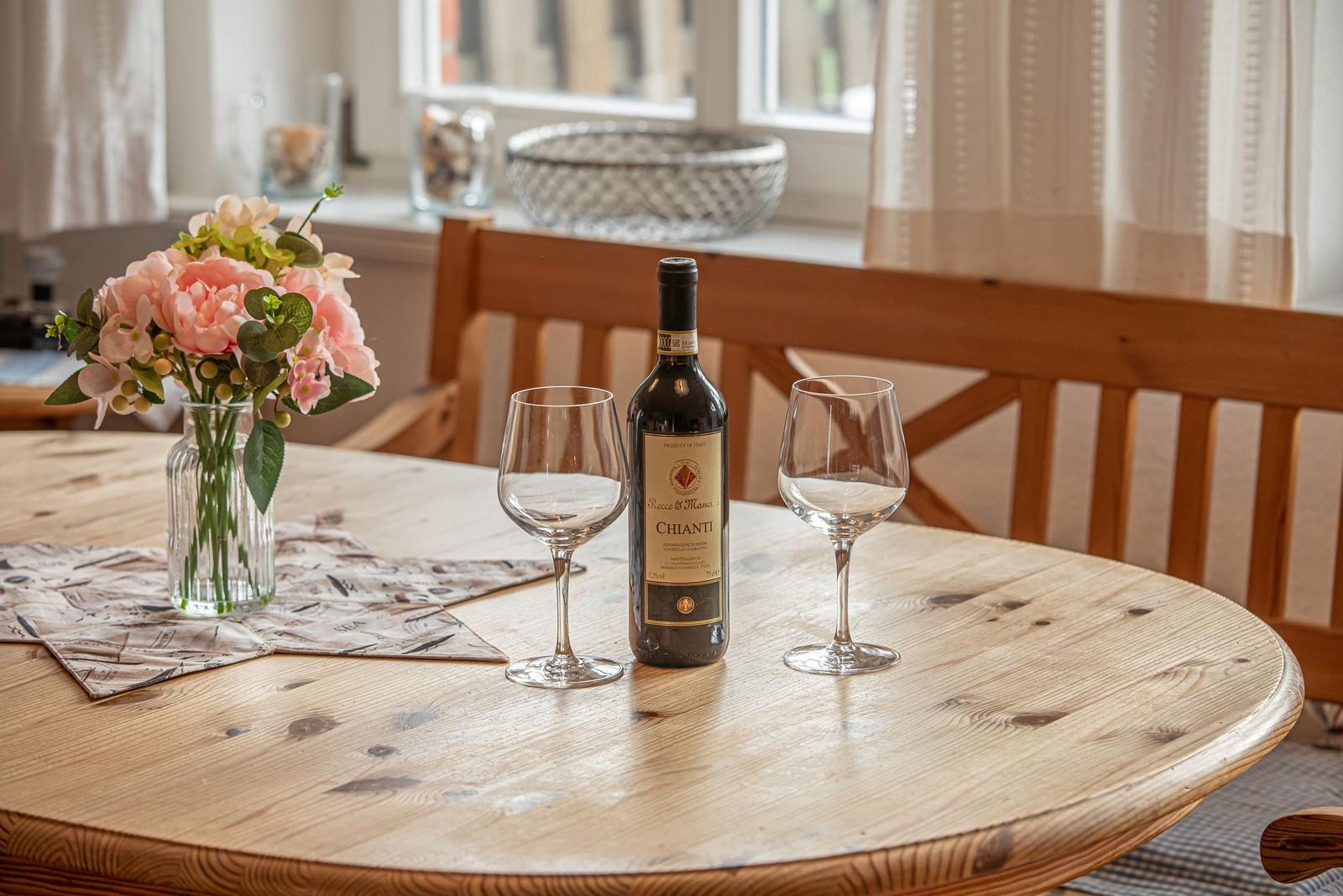 Runde Holztisch mit Weinflasche, zwei Gläsern und Blumenarrangement.