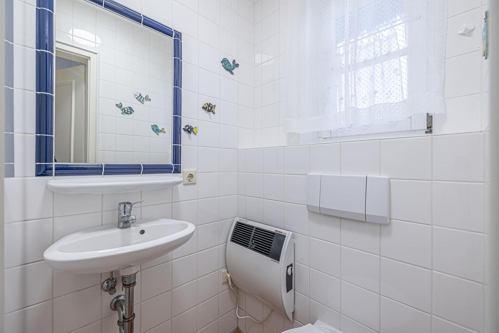Badezimmer mit Waschbecken, Spiegel und Fenster mit weißen Vorhängen.