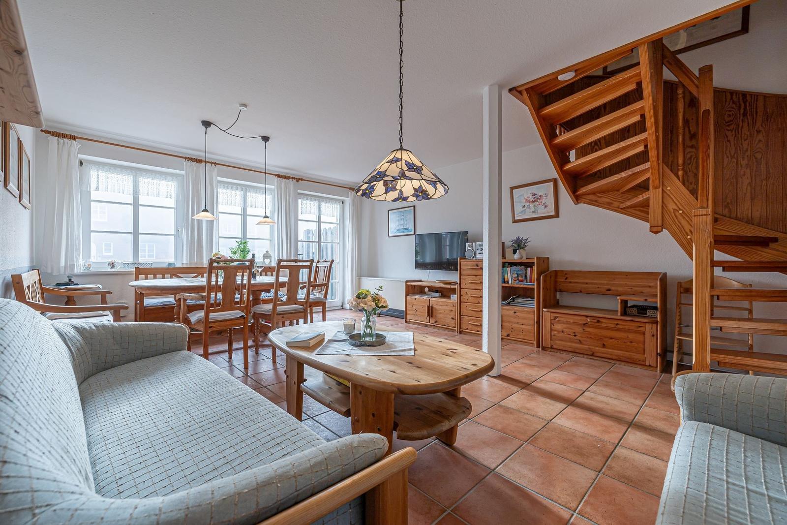 Wohn- und Essbereich mit Holzmöbeln, Terrakottboden und Treppe zur oberen Etage.