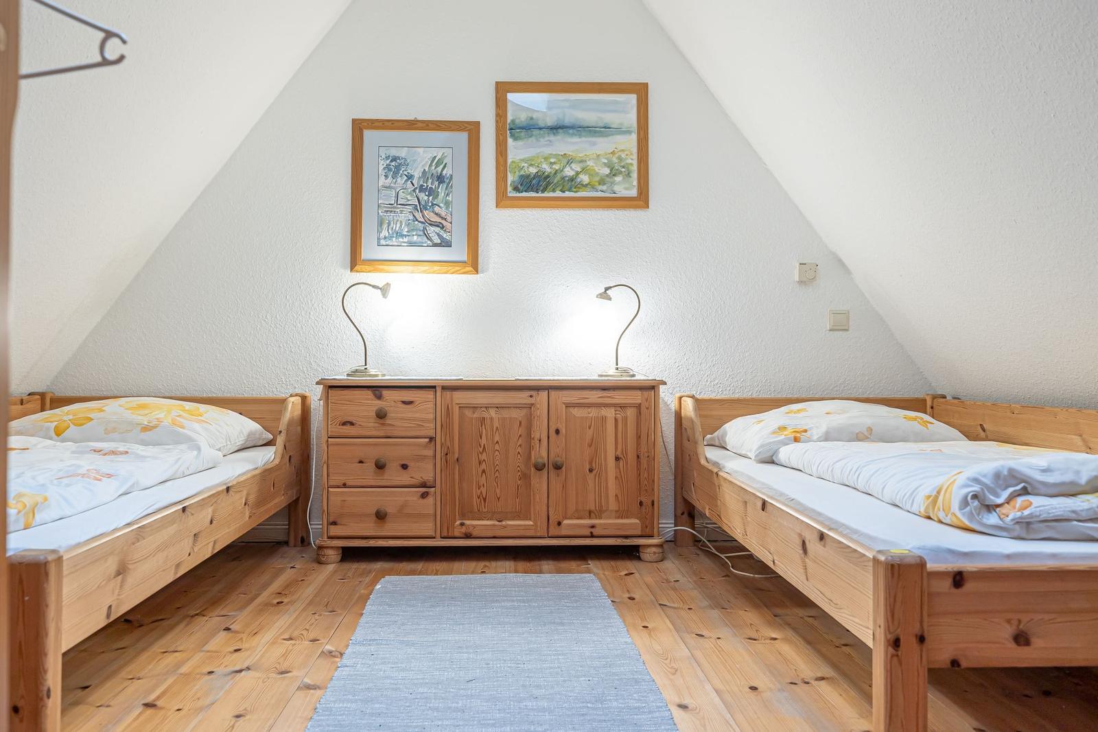 Zwei Betten mit Holzrahmen stehen gegenüber einem Schrank mit Lampen und Bildern an der Wand.