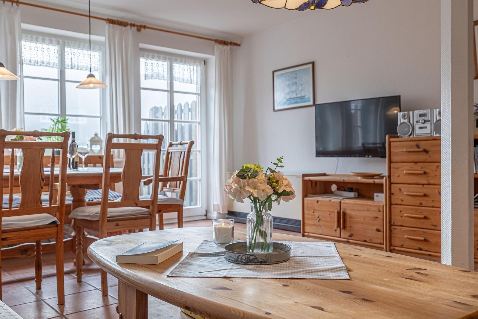 Essbereich mit Holztisch und Stühlen. Fernseher und Holzschrank im Hintergrund.