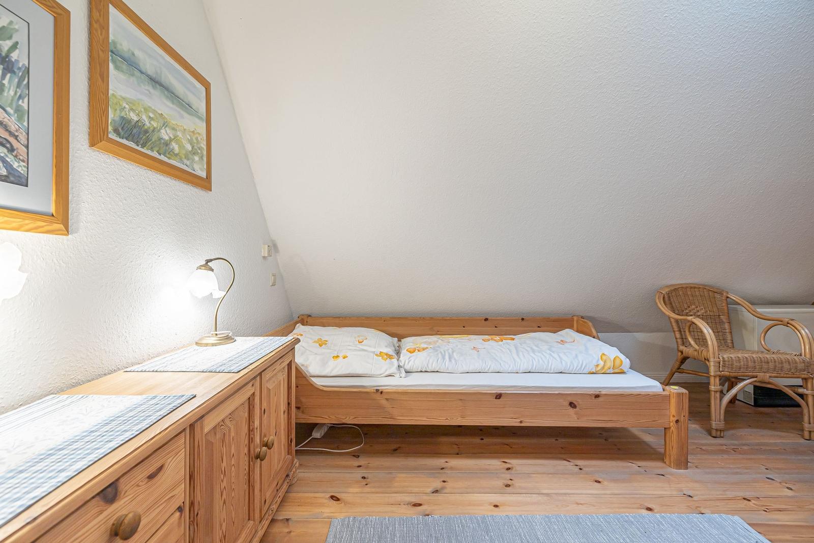 Schlafzimmer mit Holzbett, Schrank und Stuhl unter schräger Decke.