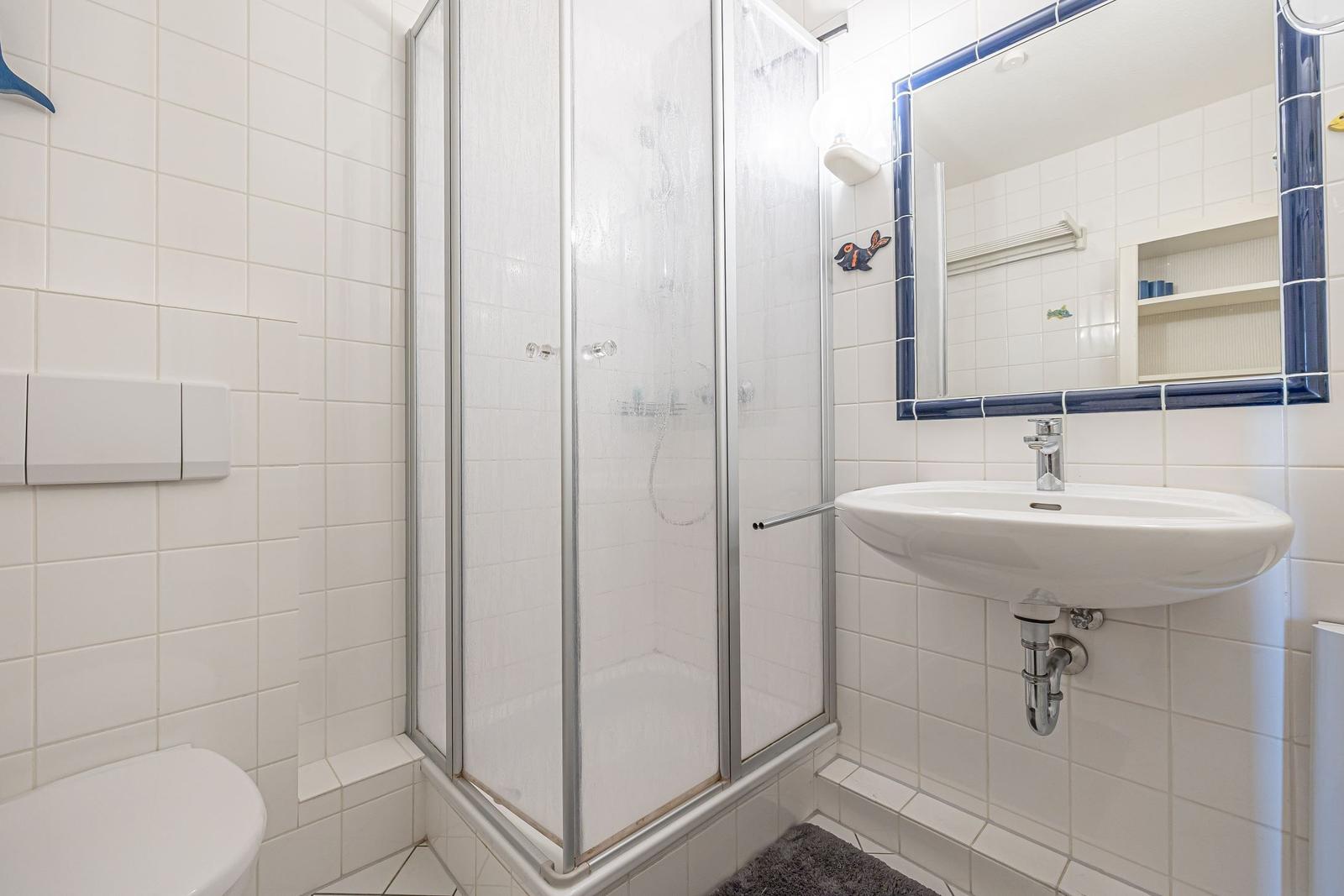 Badezimmer mit Dusche, Waschbecken und Spiegel mit blauem Rahmen.