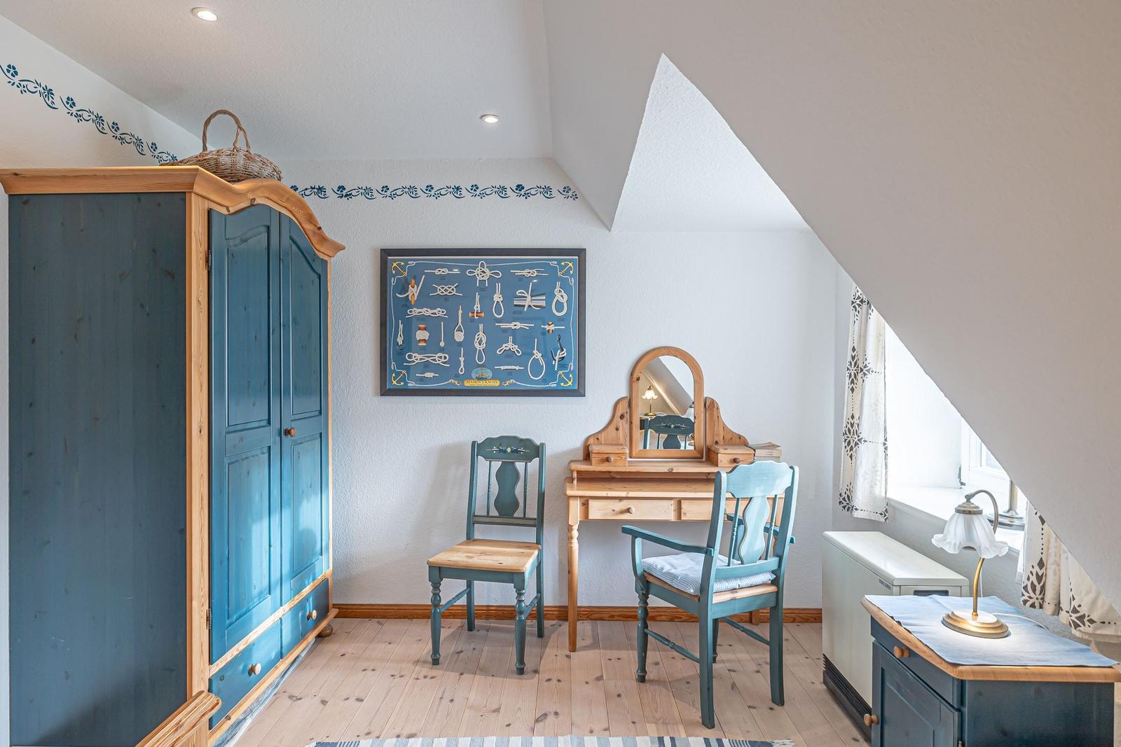 Schlafzimmer mit Kleiderschrank, Schreibtisch und Stühlen unter Dachschrägen.