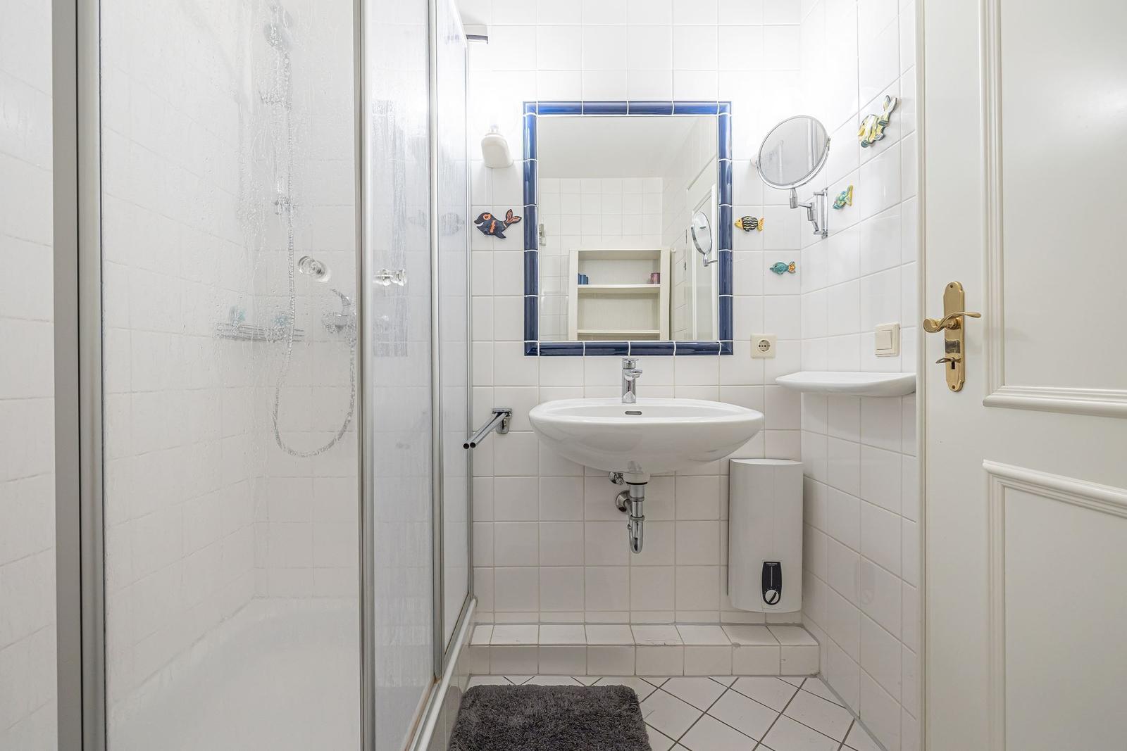 Badezimmer mit Dusche, Waschbecken und Spiegel mit blauem Rahmen.