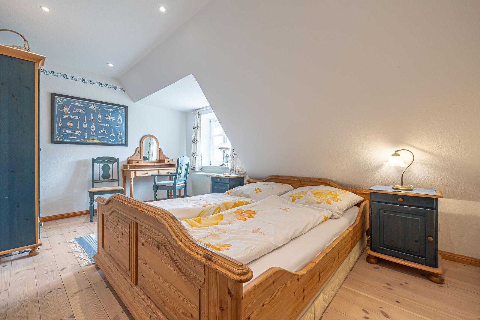 Schlafzimmer mit Holzbett, Schminktisch und Kleiderschrank unter schrägem Dach.