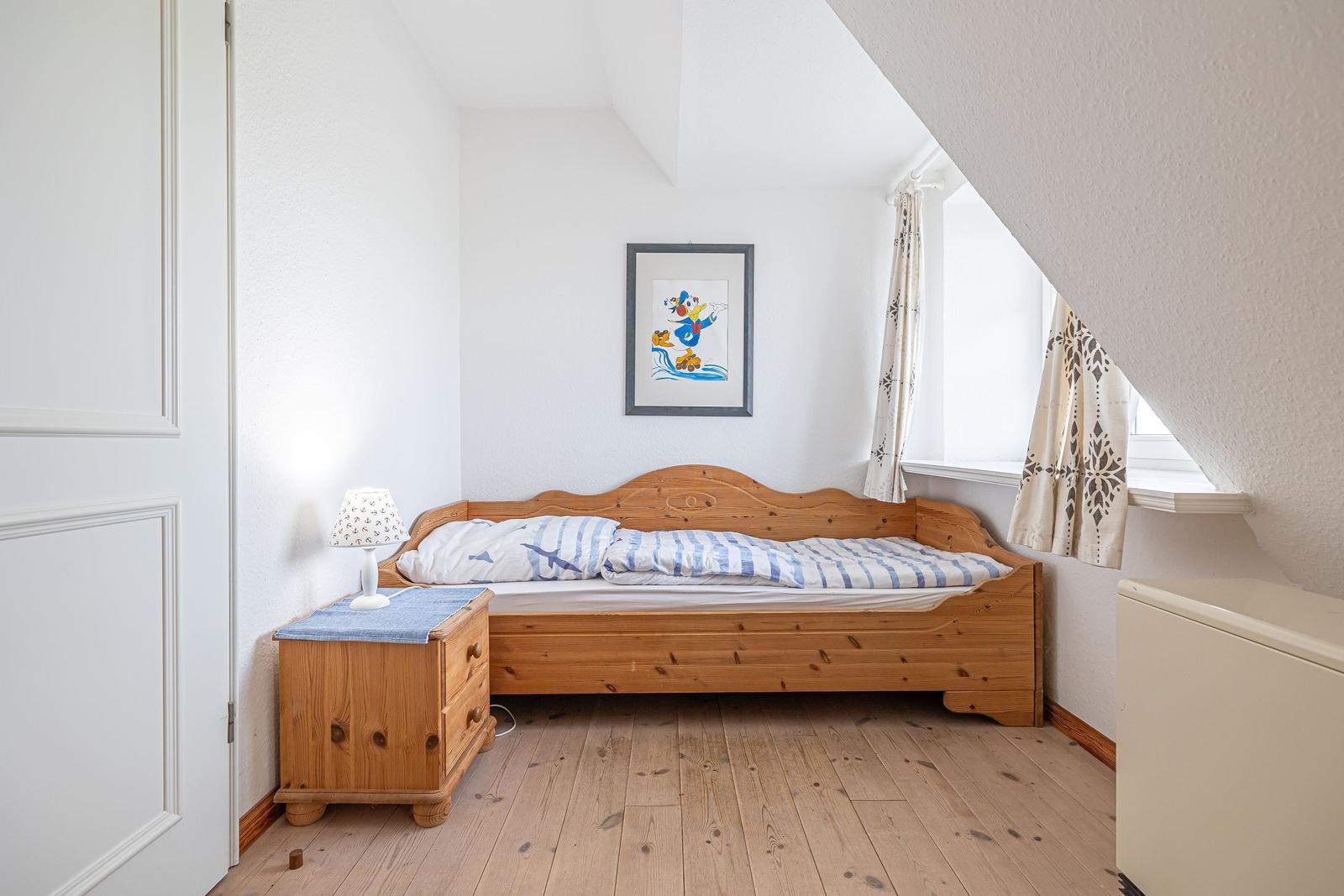 Ein Schlafzimmer mit Holzbett, Nachttisch und Fenster unter Dachschrägen.