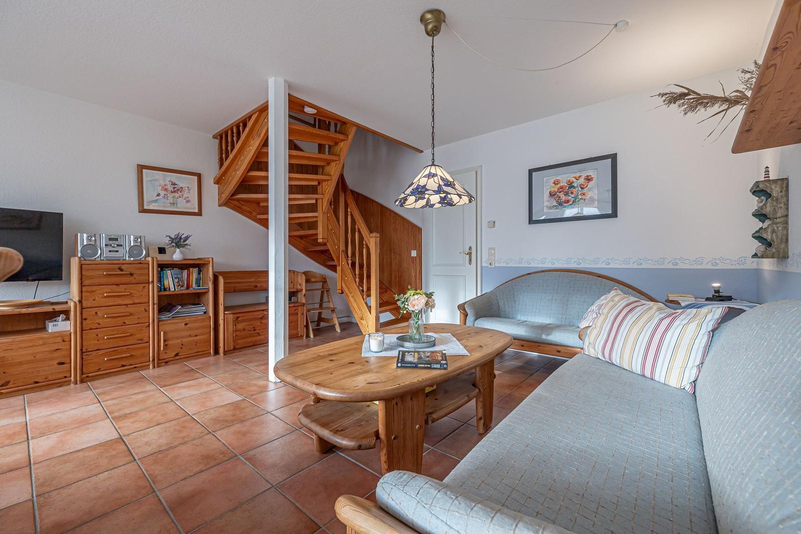 Wohnzimmer mit Holztreppe, Sofa und Esstisch. Terrakottaboden und Holzmöbel.