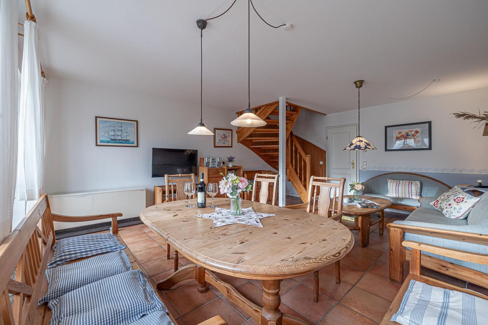 Esszimmer mit Holztisch, Stühlen und Sofa. Treppenhaus im Hintergrund.