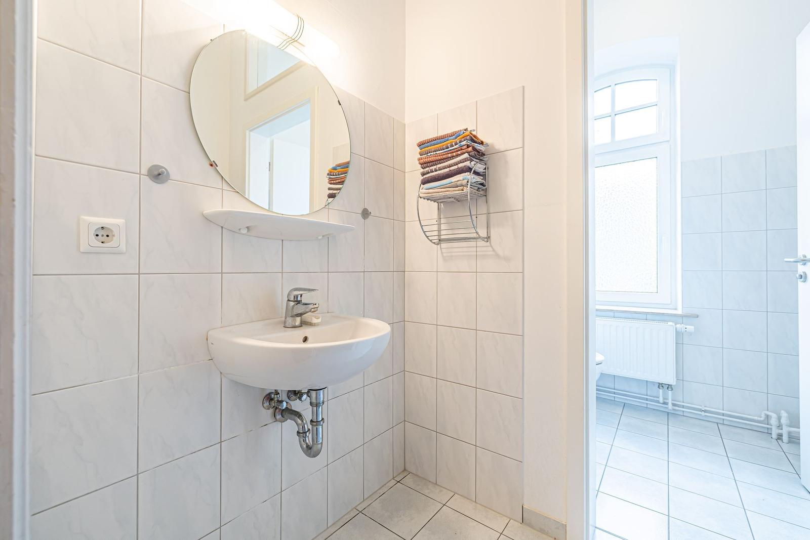 Badezimmer mit Waschbecken, Spiegel und Handtuchhalter. Durchgang zur Toilette.