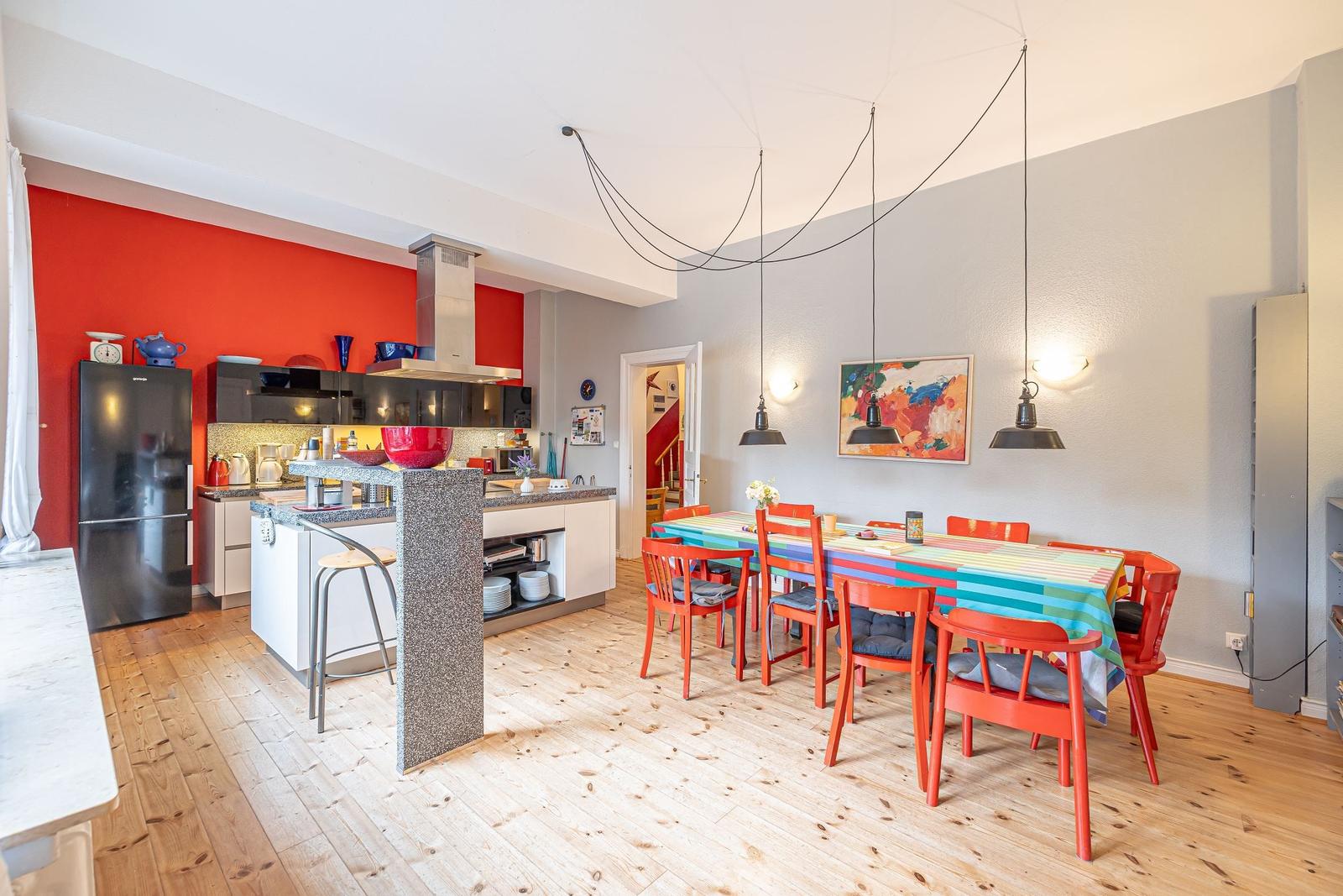Küche mit Essbereich, rote Wand, farbiger Tisch und Stühle.