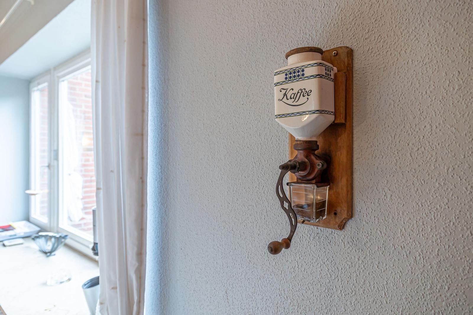 Wandmontierte Kaffeemühle mit Kaffeefass und Handkurbel.